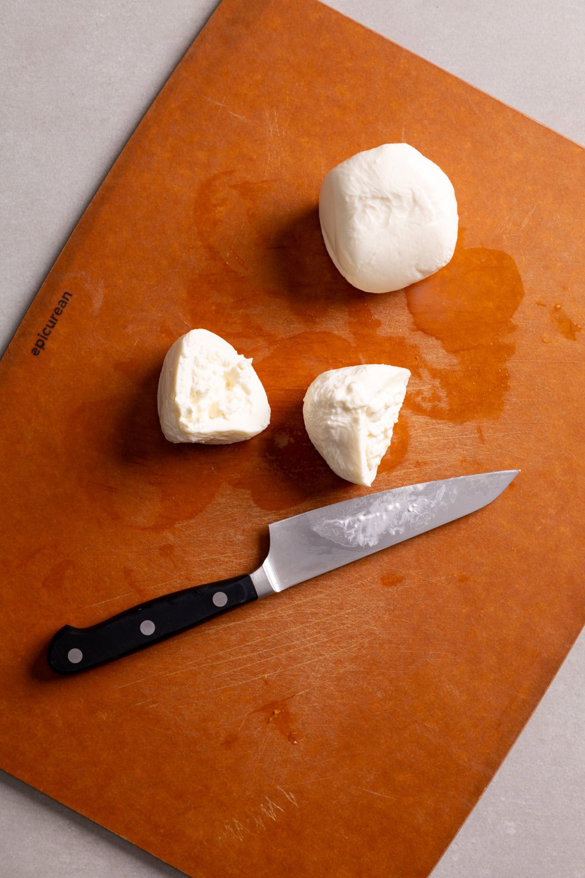 Burrata cheese getting sliced on a cutting board.