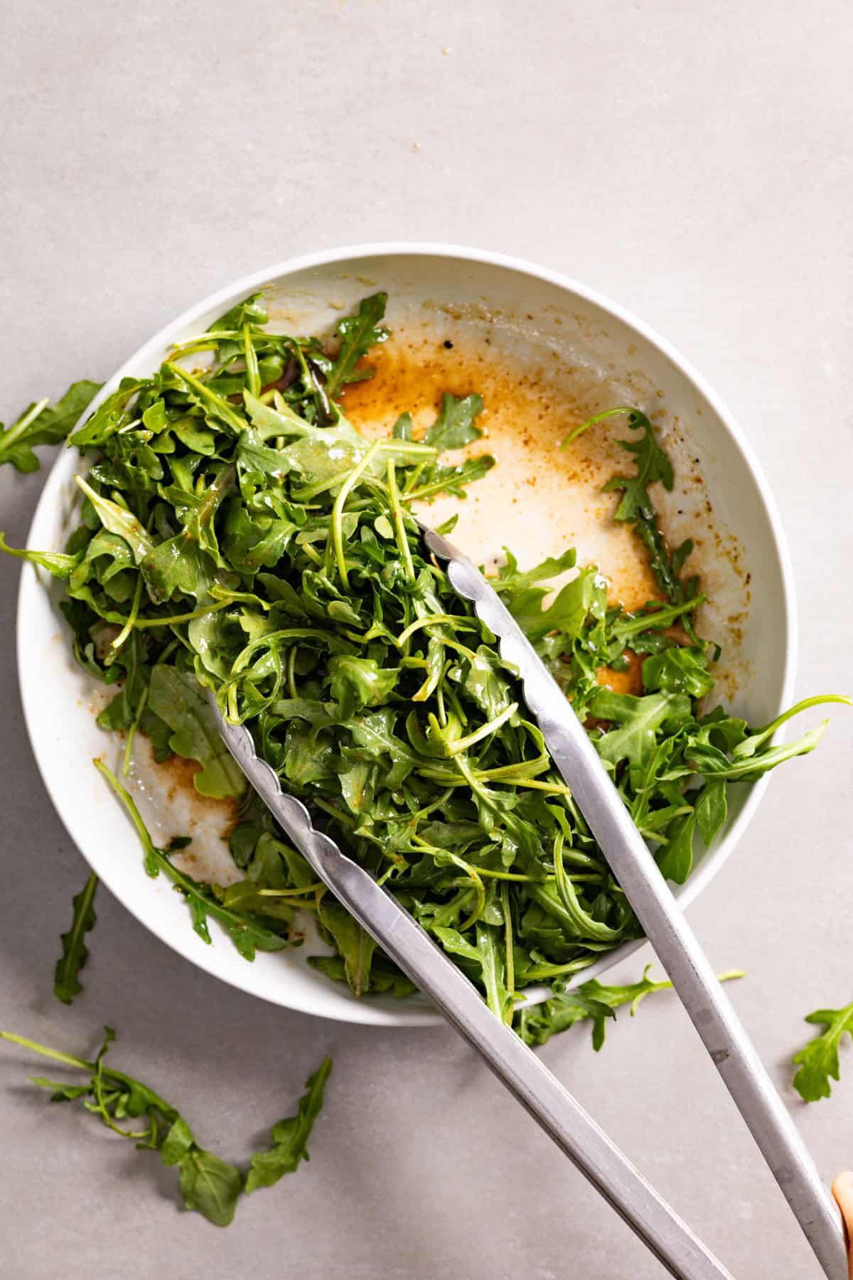 Arugula getting tossed in a bowl with balsamic vinaigrette.