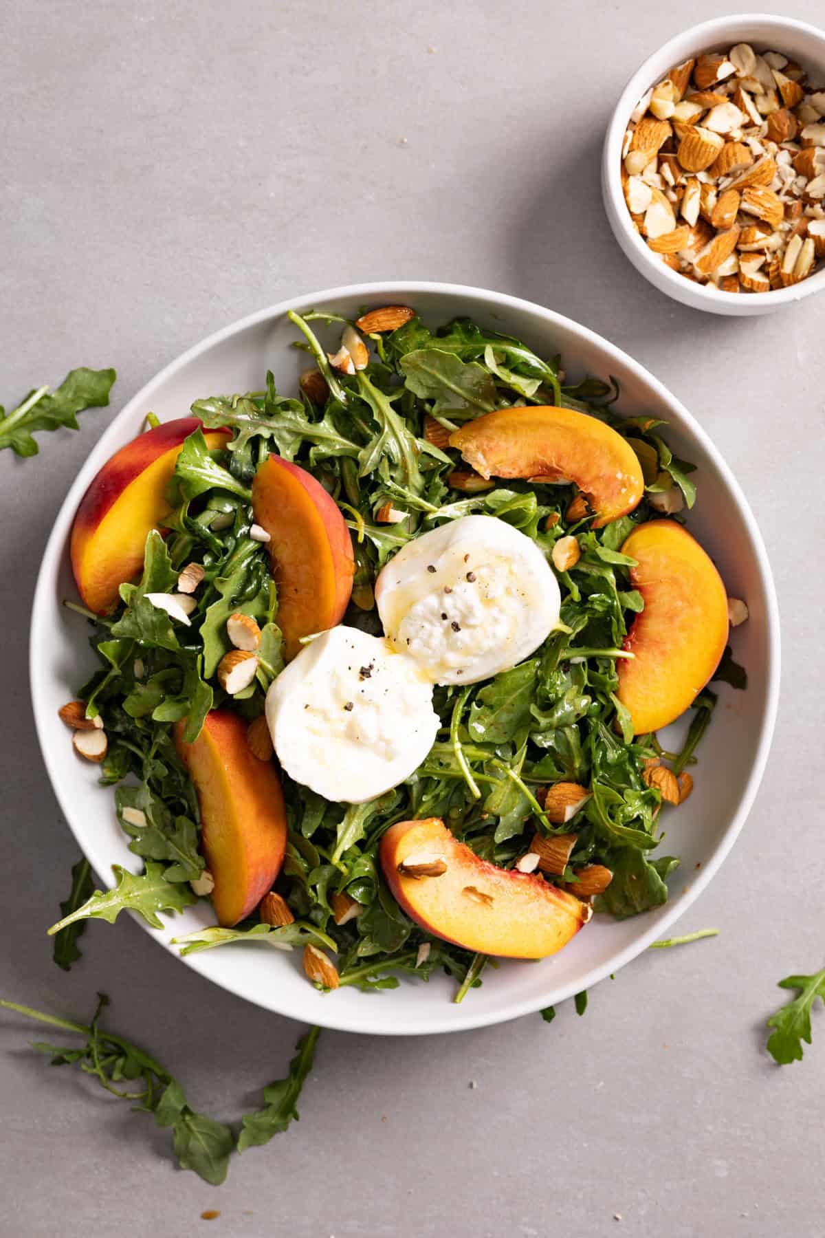 Arugula burrata salad in a bowl topped with peaches and almonds.