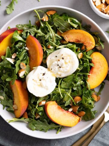 Close up of a serving of arugula burrata salad with peaches and almonds.