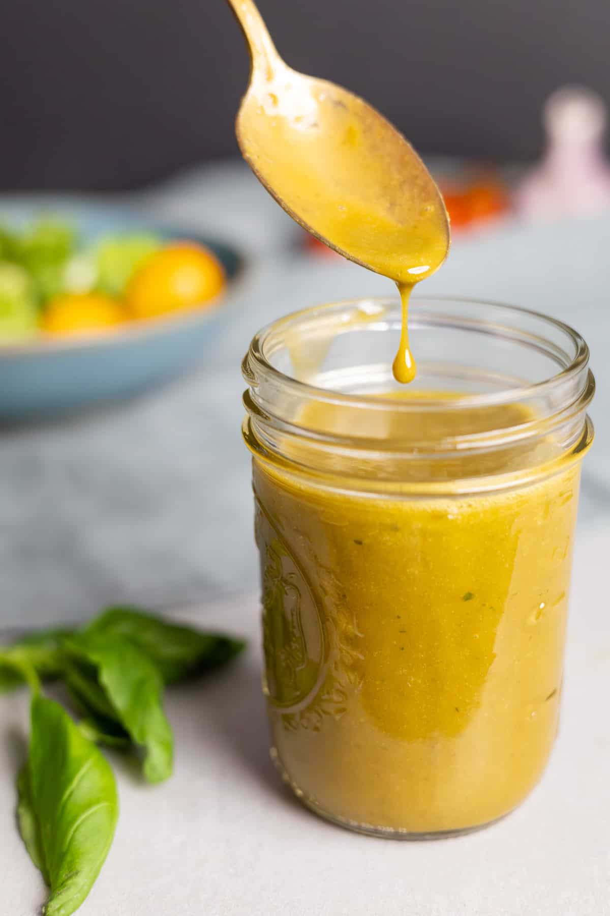 A spoon dripping creamy basil balsamic vinaigrette into a mason jar.