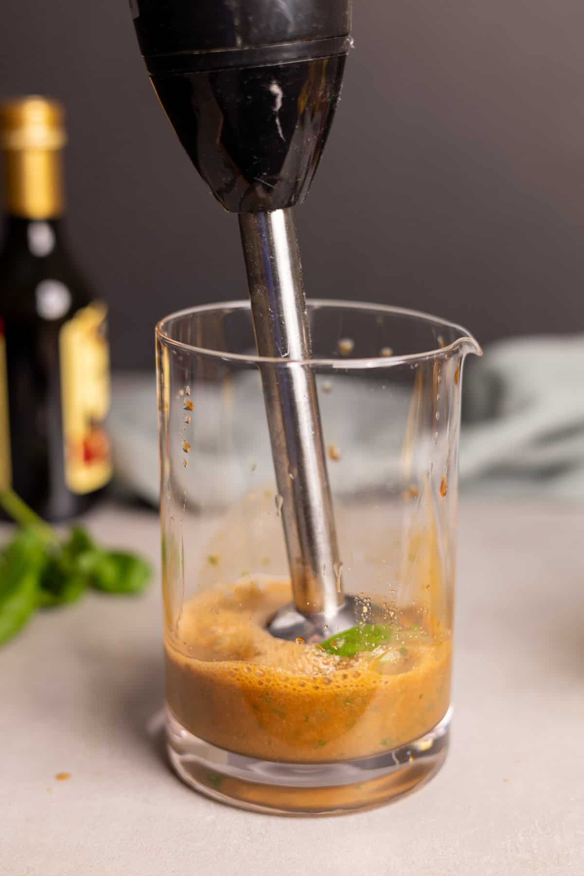 Ingredients for basil balsamic vinaigrette in a glass jar with an immersion blender mixing up the ingredients.
