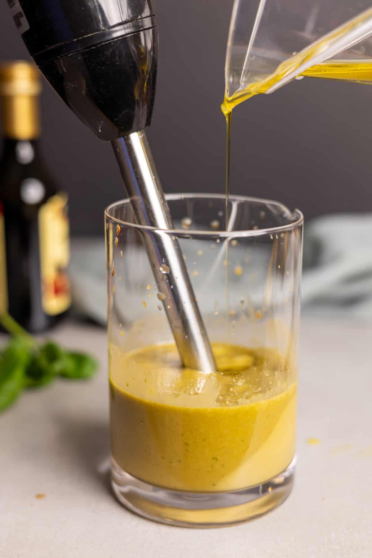 Oil drizzling into basil balsamic vinaigrette as an immersion blender blends the dressing.
