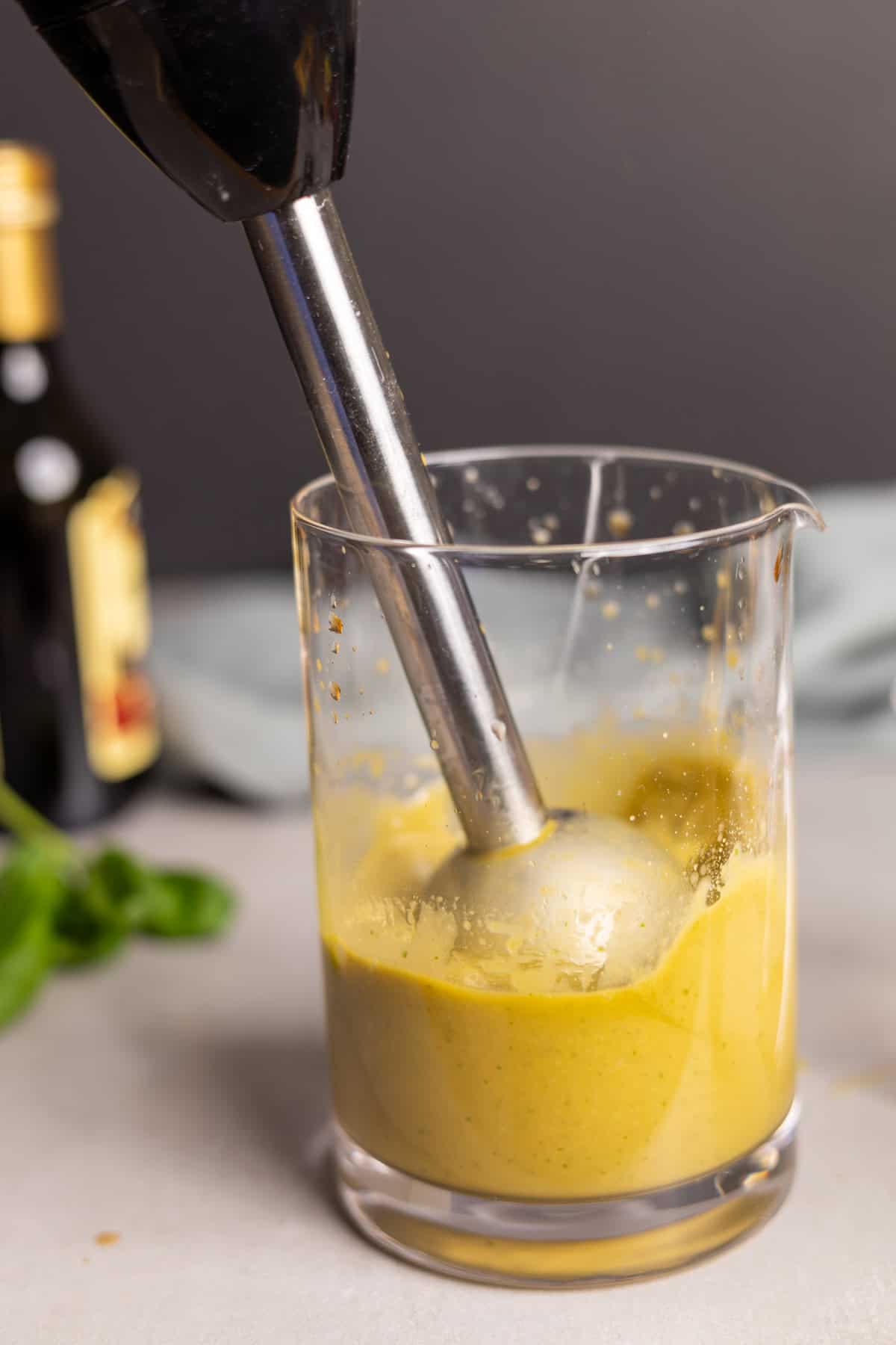 Basil balsamic vinaigrette getting emulsified by an immersion blender in a glass jar.
