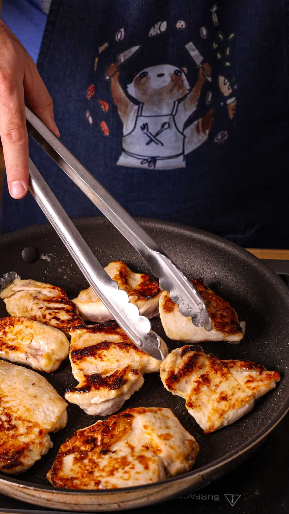 Sliced chicken breasts getting seared in a nonstick skillet.
