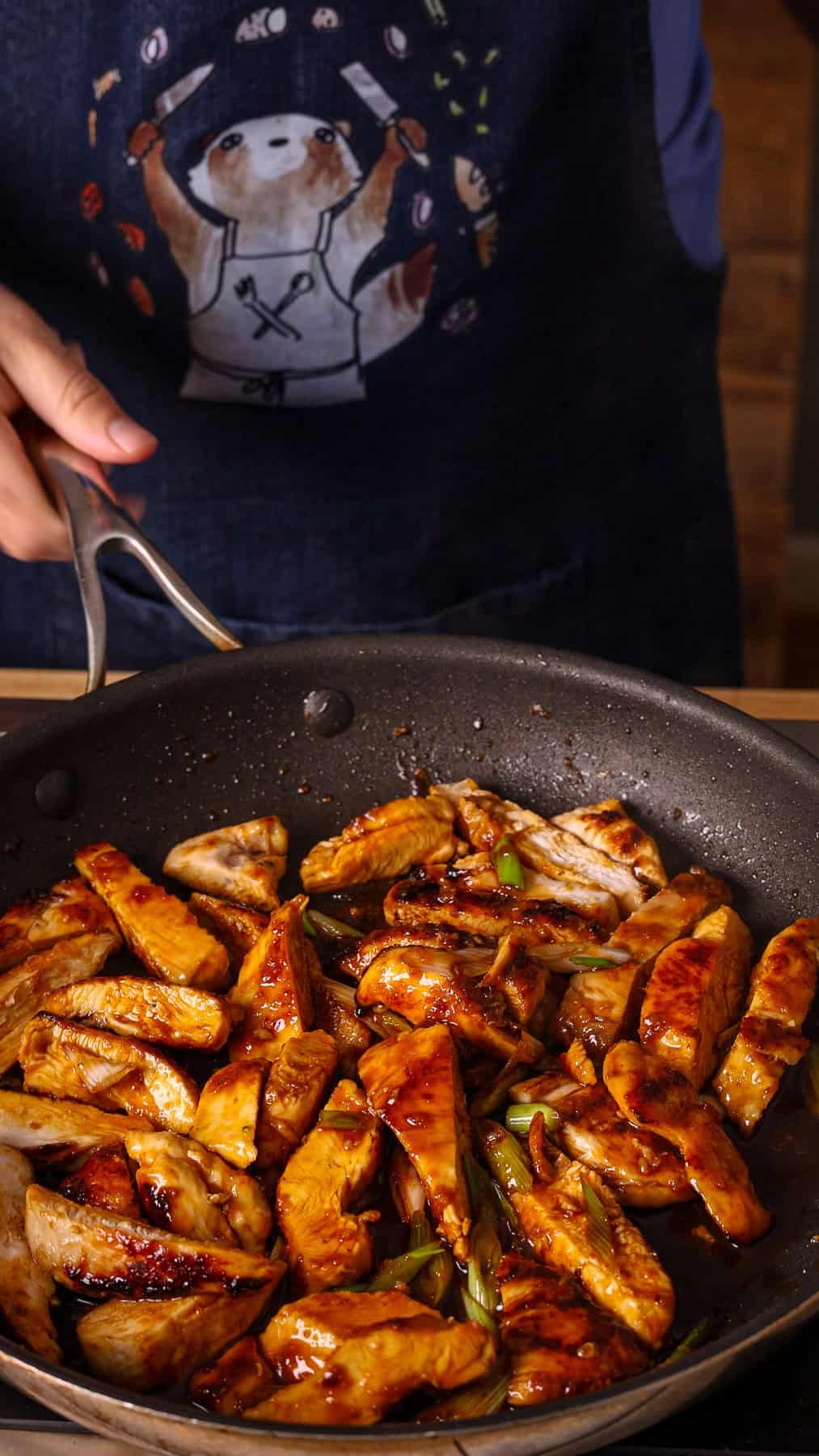 Sliced cooked chicken breasts getting tossed in a honey ginger sauce in a nonstick skillet.