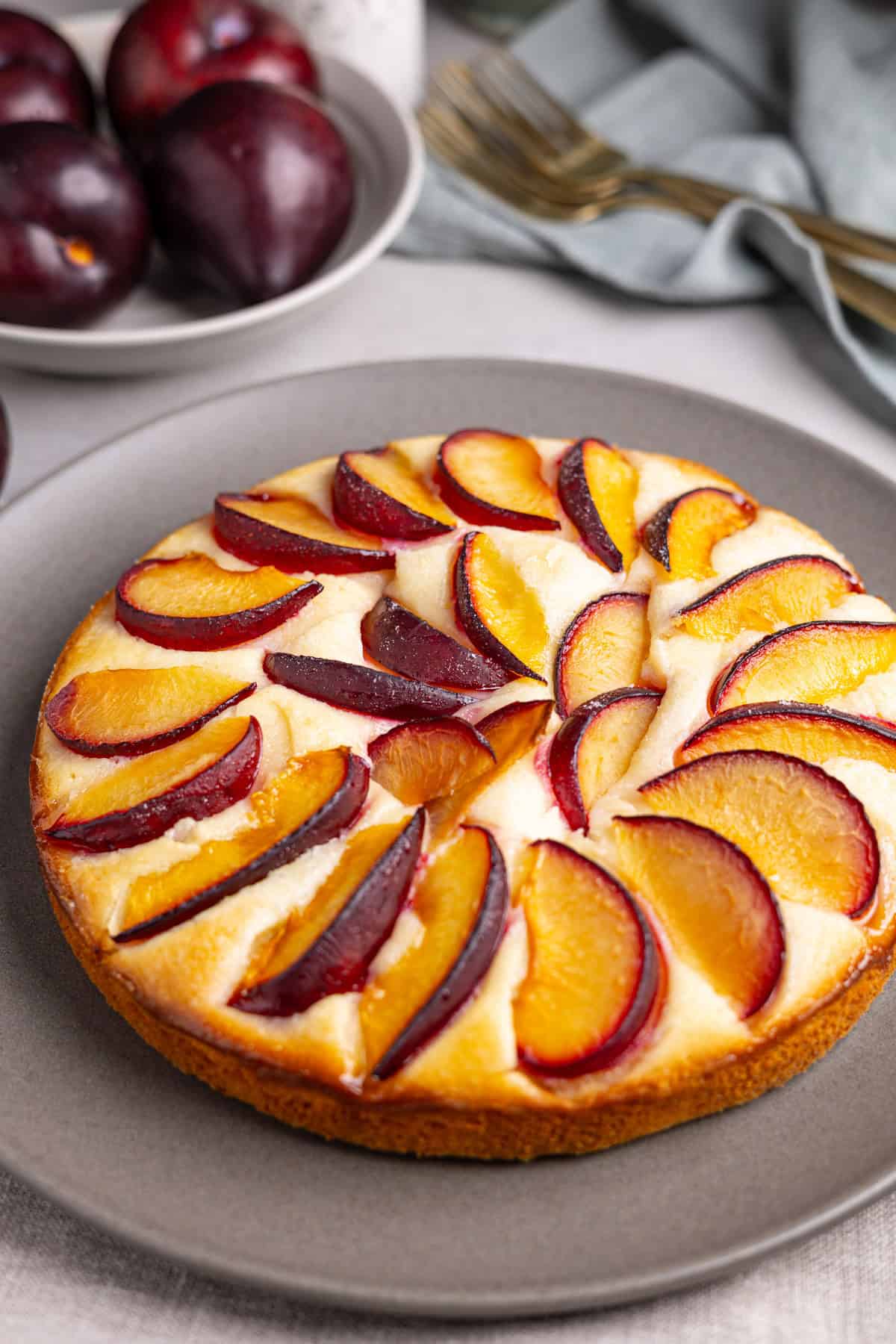 Plum yogurt cake on a gray plate with plums in the background.