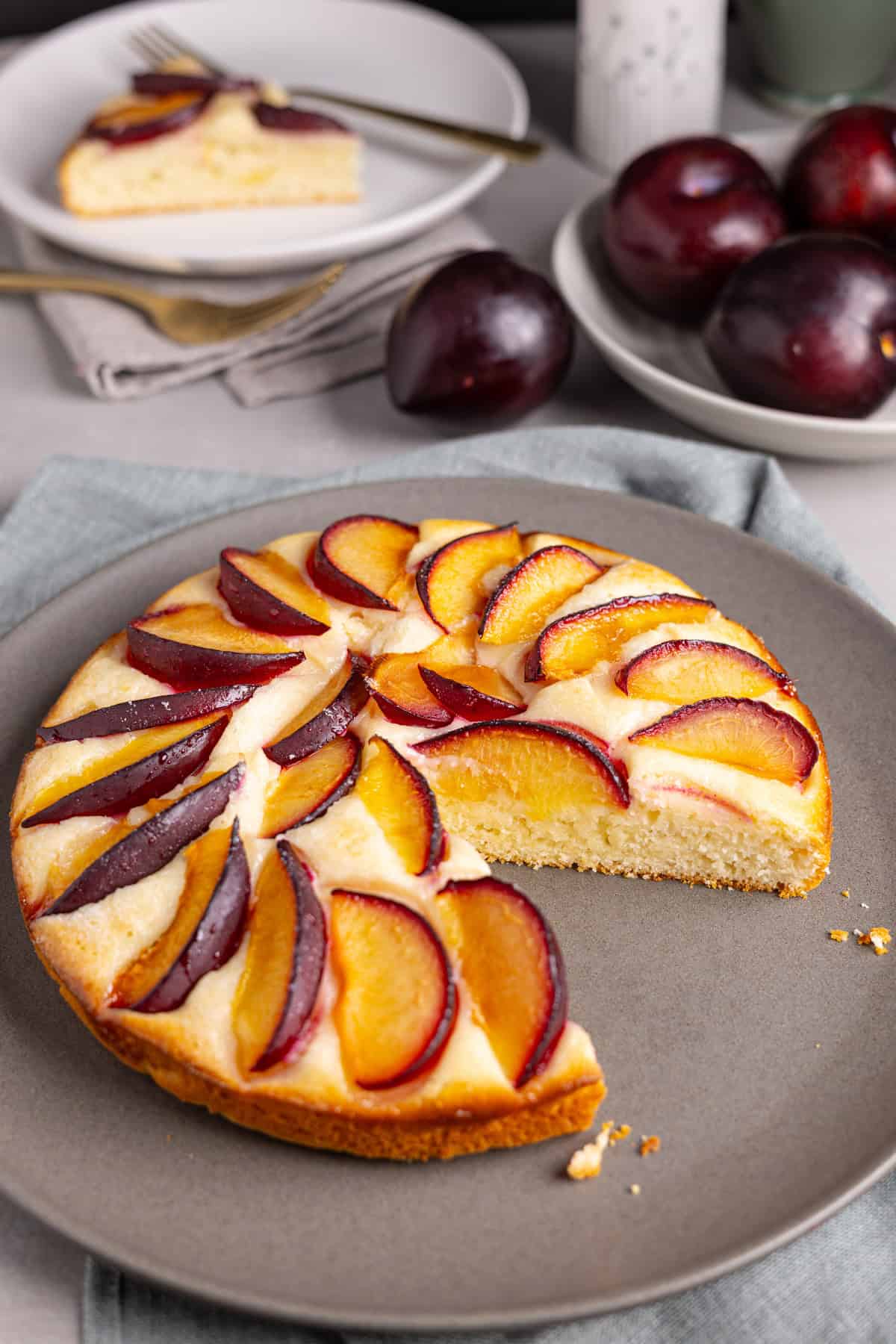 A plum yogurt cake on a plate with a slice taken out and in the background.