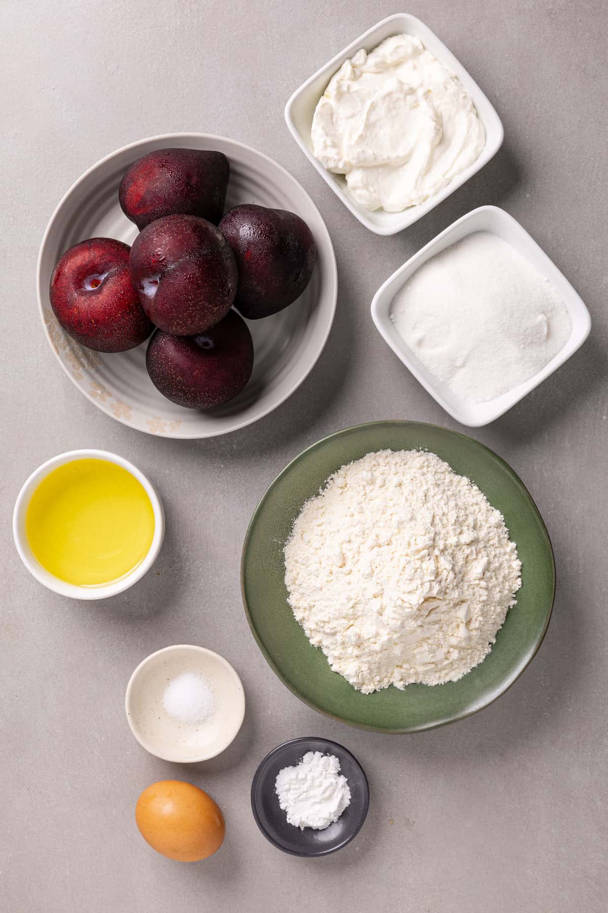 Ingredients for plum yogurt cake on a gray table.