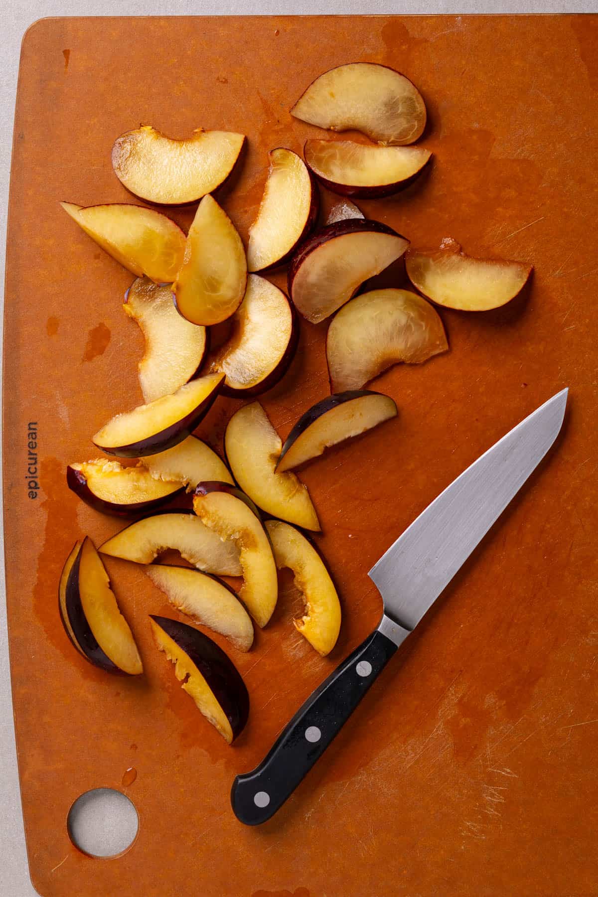 Sliced plums on a cutting board with a small knife to the side.