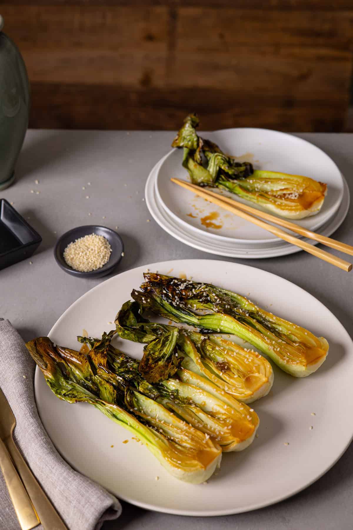 A platter of roasted bok choy and a small serving in the background with chop sticks.