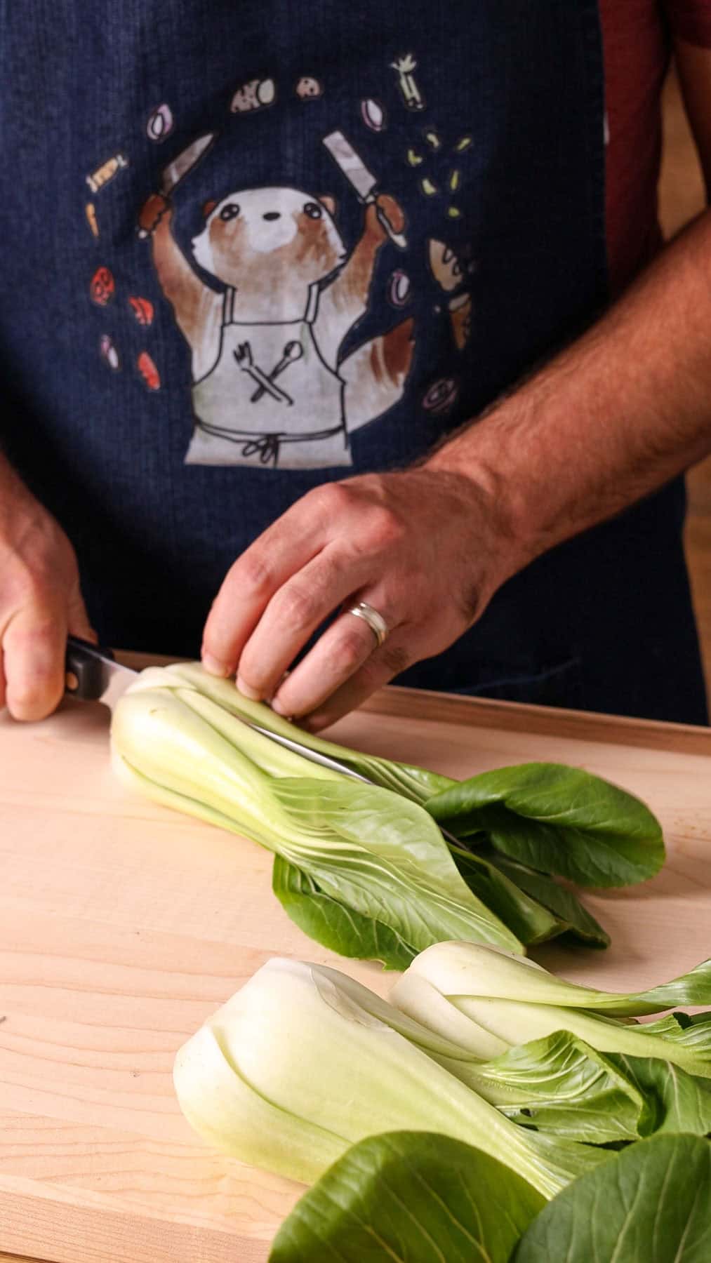 Baby bok choy getting cut in half on a wooden cutting board.