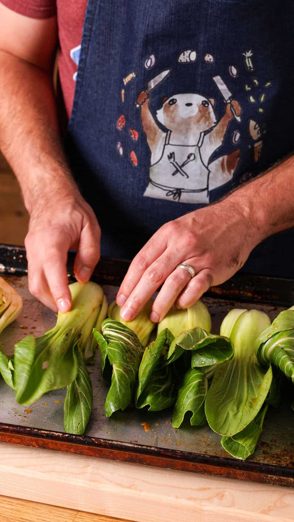 Baby bok choy in a soy ginger sauce getting layer on a baking sheet to roast.