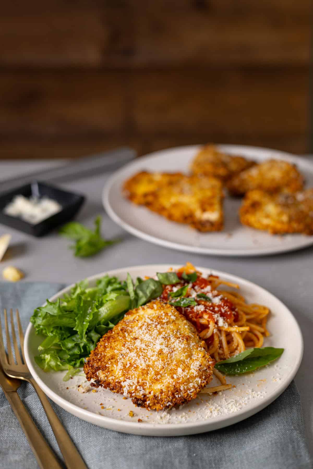 A plate with crispy air fryer parmesan crusted chicken, spaghetti, tomato sauce, and salad on a butcher block countertop.