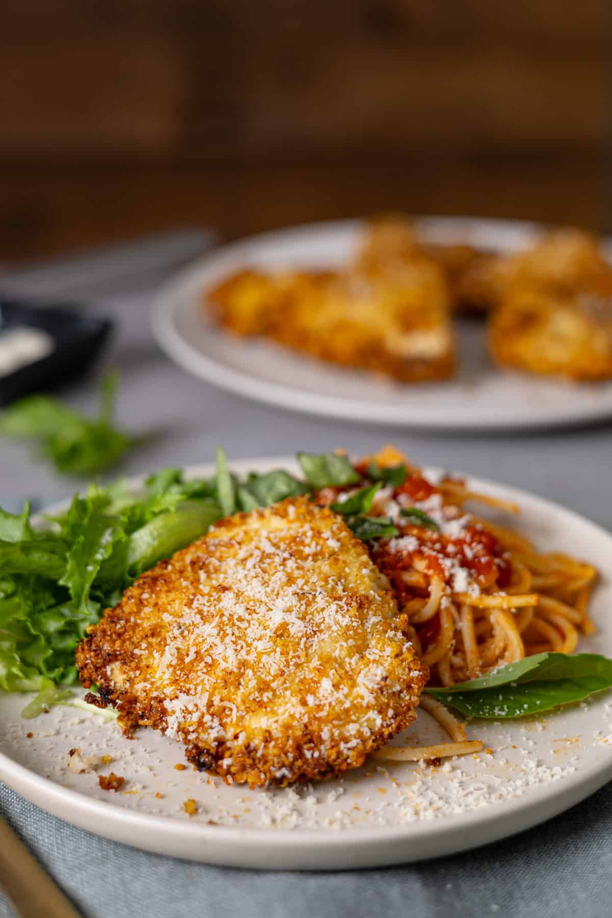 A closeup of crispy air fryer parmesan chicken with pasta, sauce, and salad on a plate.