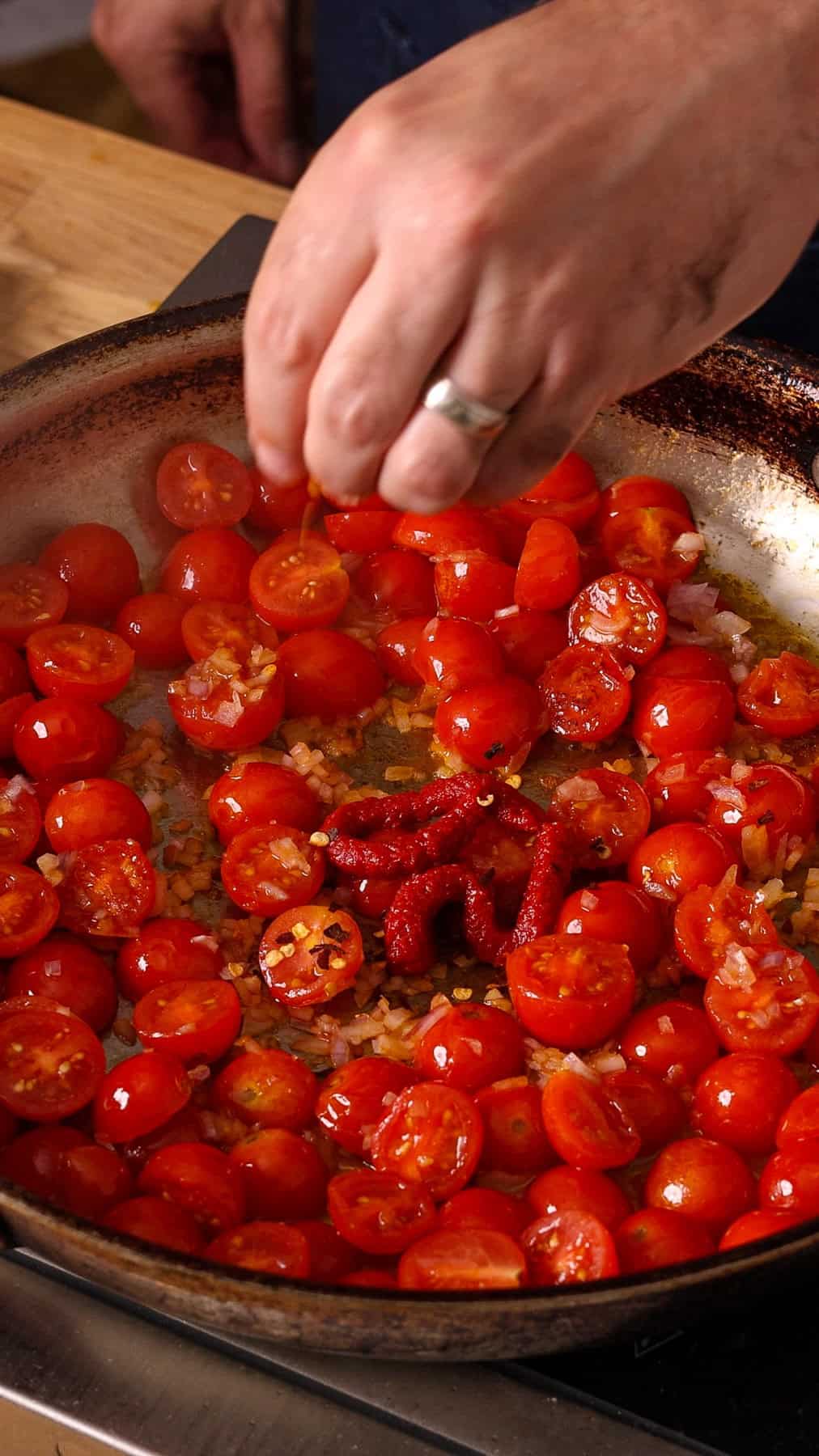 Tomato paste and aromatics getting added to a skillet with cooked cherry tomatoes.