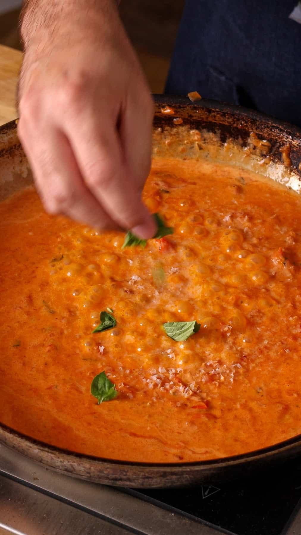 Parmesan cheese and torn basil leaves getting added to a skillet with cherry tomato sauce.