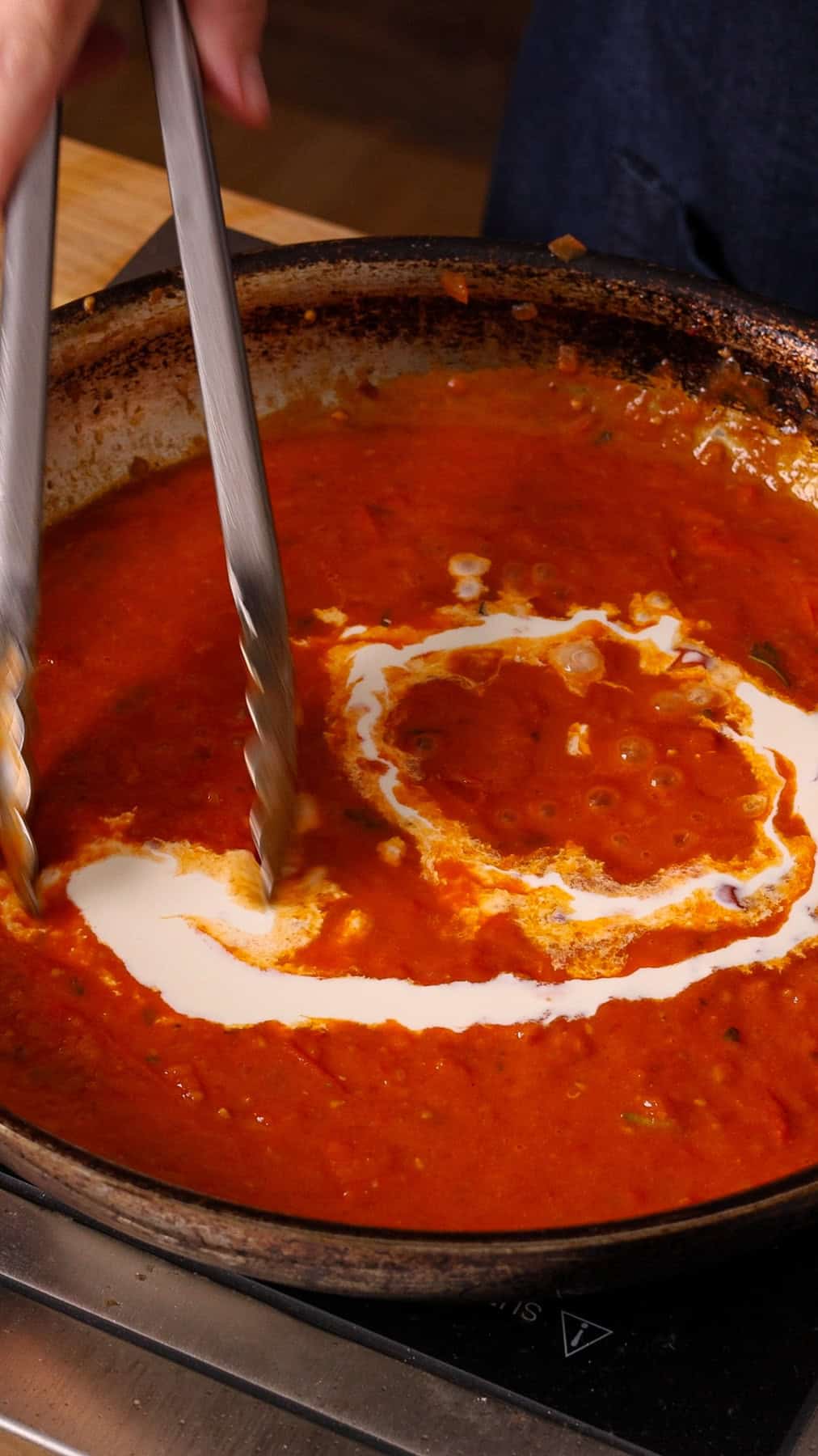 Heavy cream getting poured into a large skillet with mashed cooked cherry tomatoes.