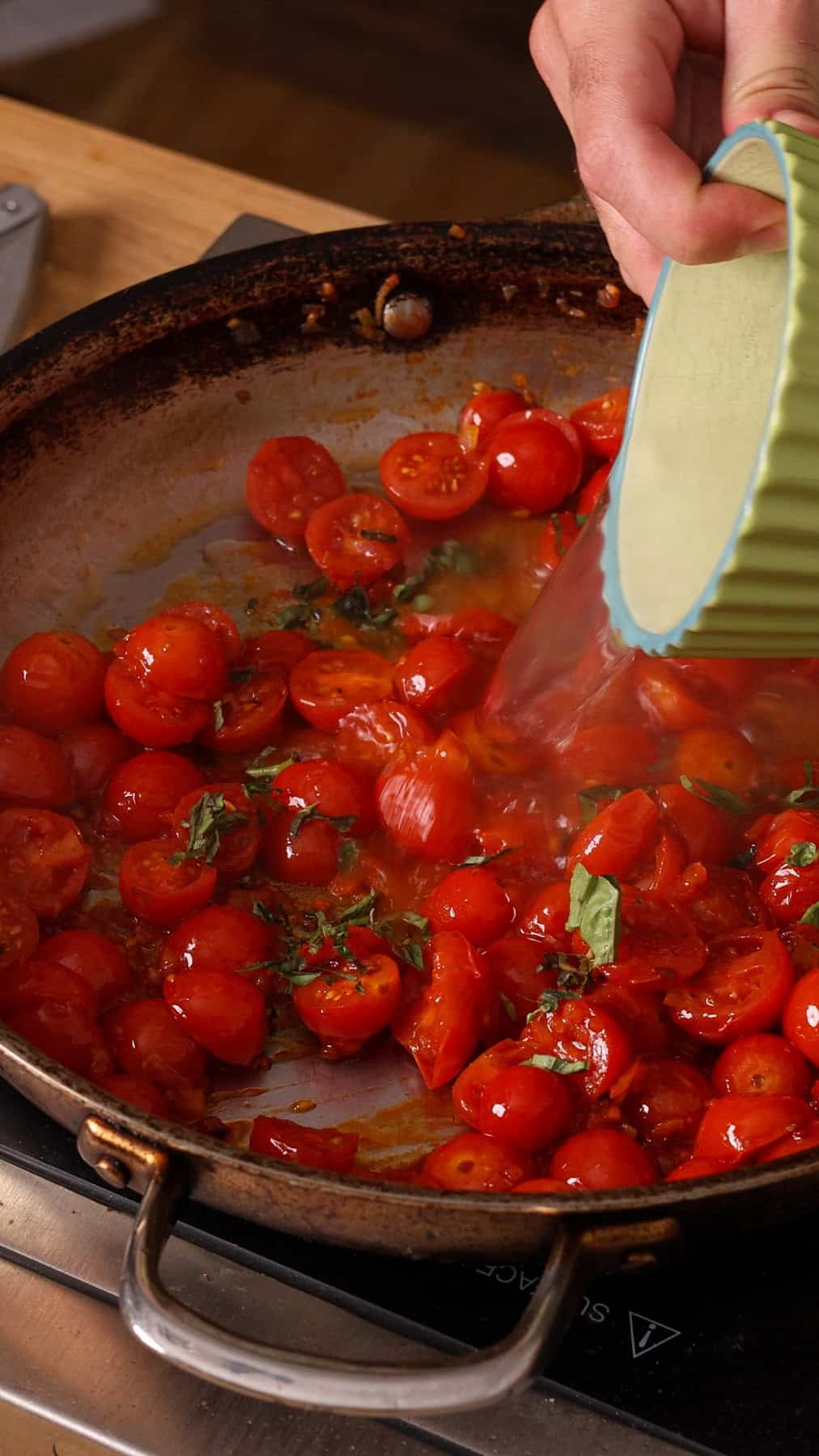 Pasta cooking liquid getting poured into a skillet with cooked cherry tomatoes for a spaghetti sauce.