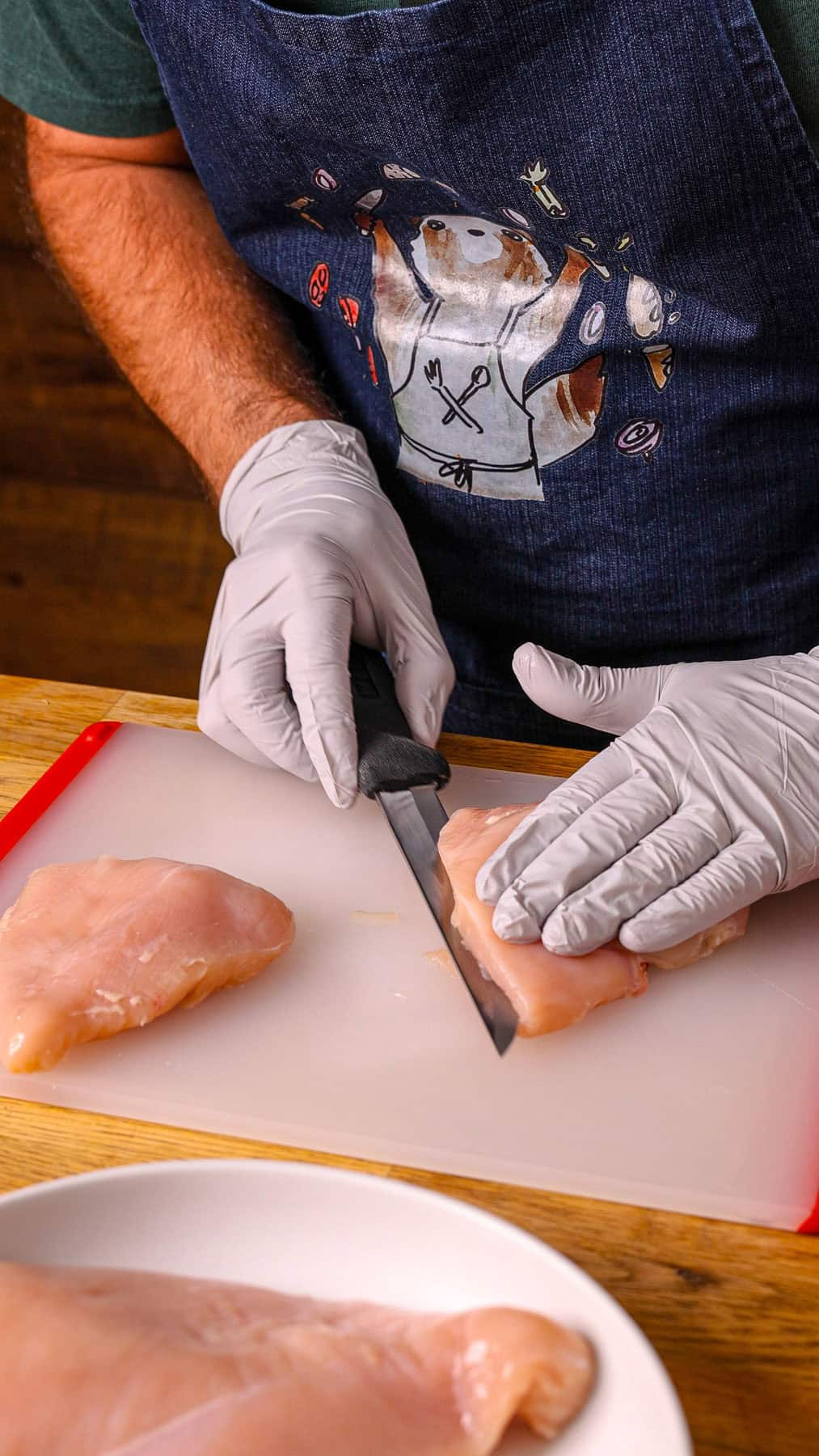 Chicken breasts getting trimmed on a cutting board.