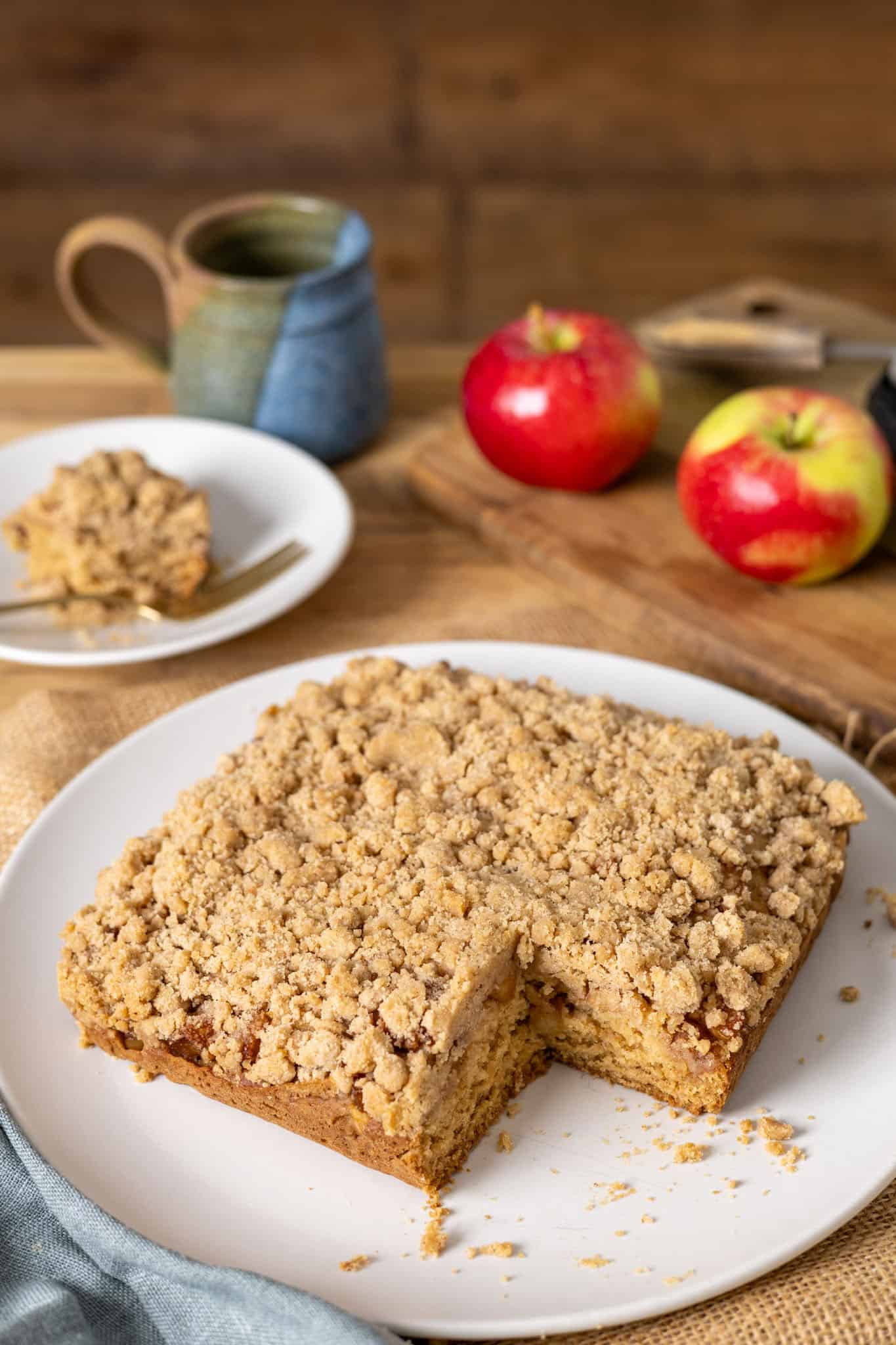 Applesauce crumb cake on a white plate with a piece taken out and on a small plate in the background.