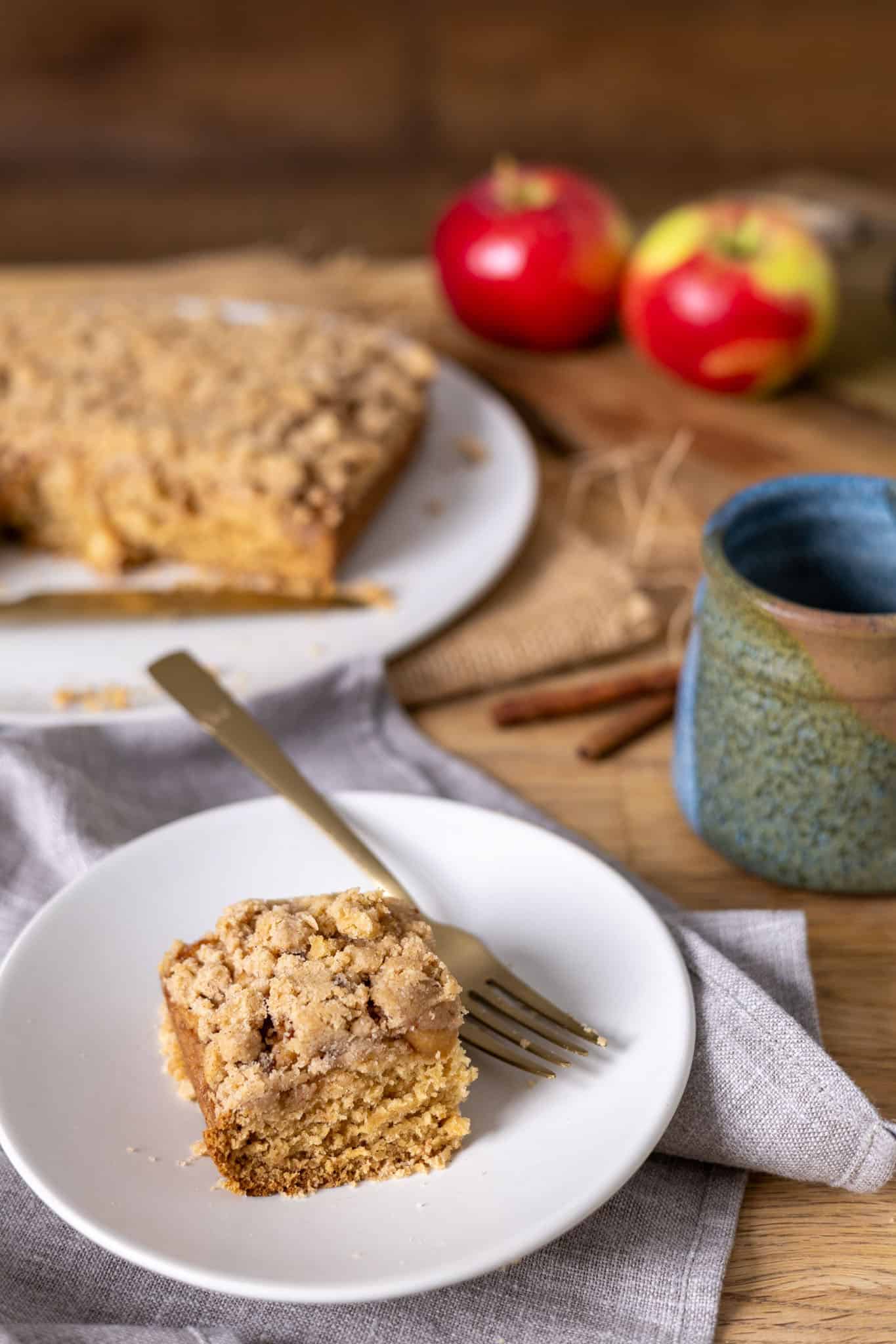 A slice of applesauce crumb cake on a small plate with the rest of the cake in the background.