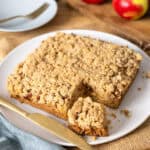 Applesauce crumb cake with a slice taken out on a white plate.