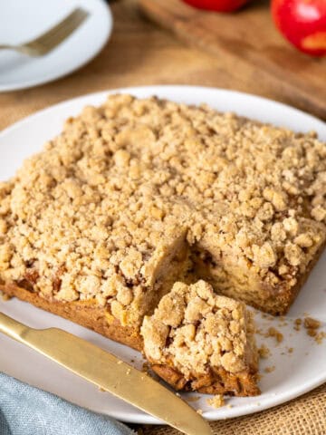 Applesauce crumb cake with a slice taken out on a white plate.