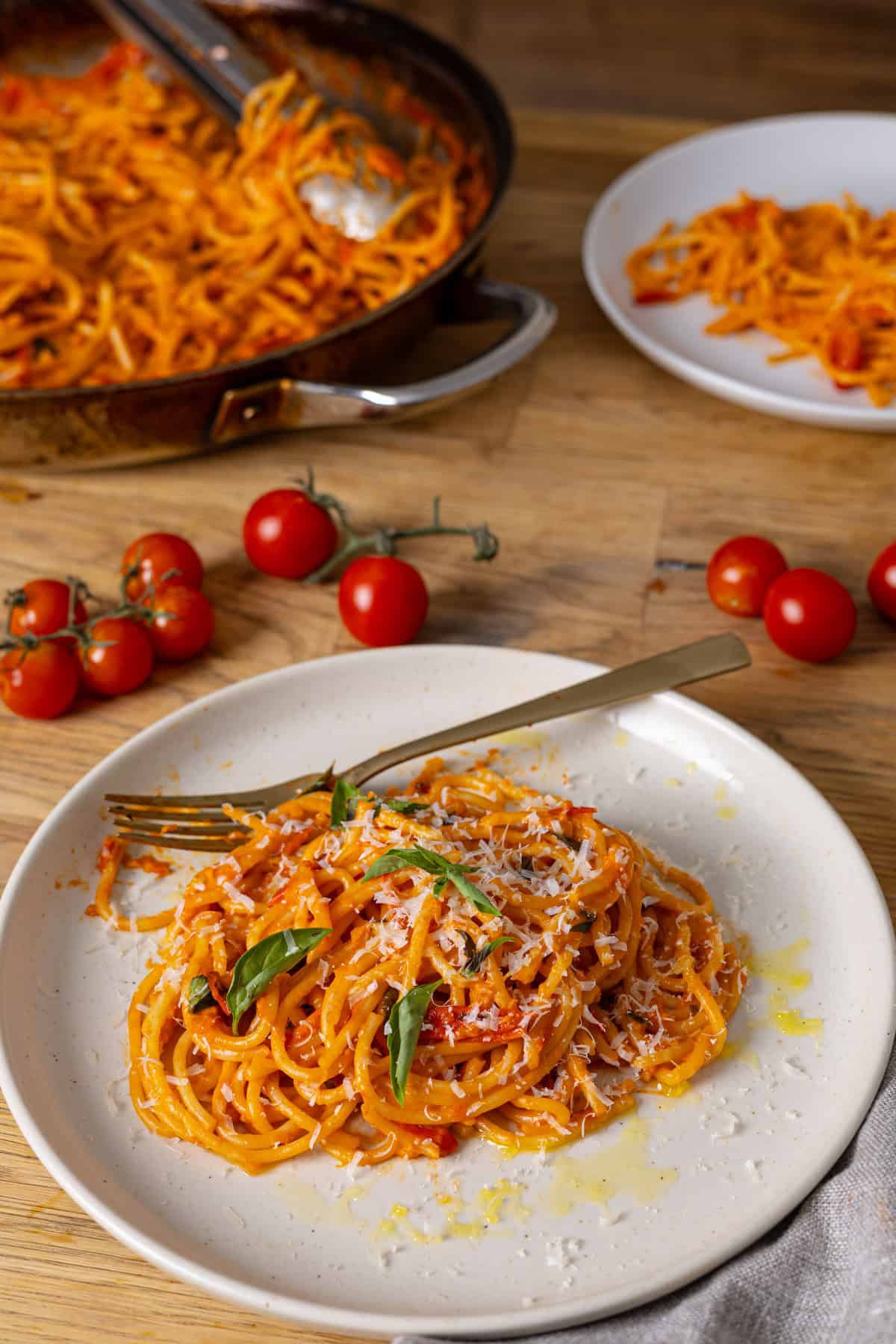 A serving of cherry tomato sauce with spaghetti on a small plate and a skillet with more pasta in the background.