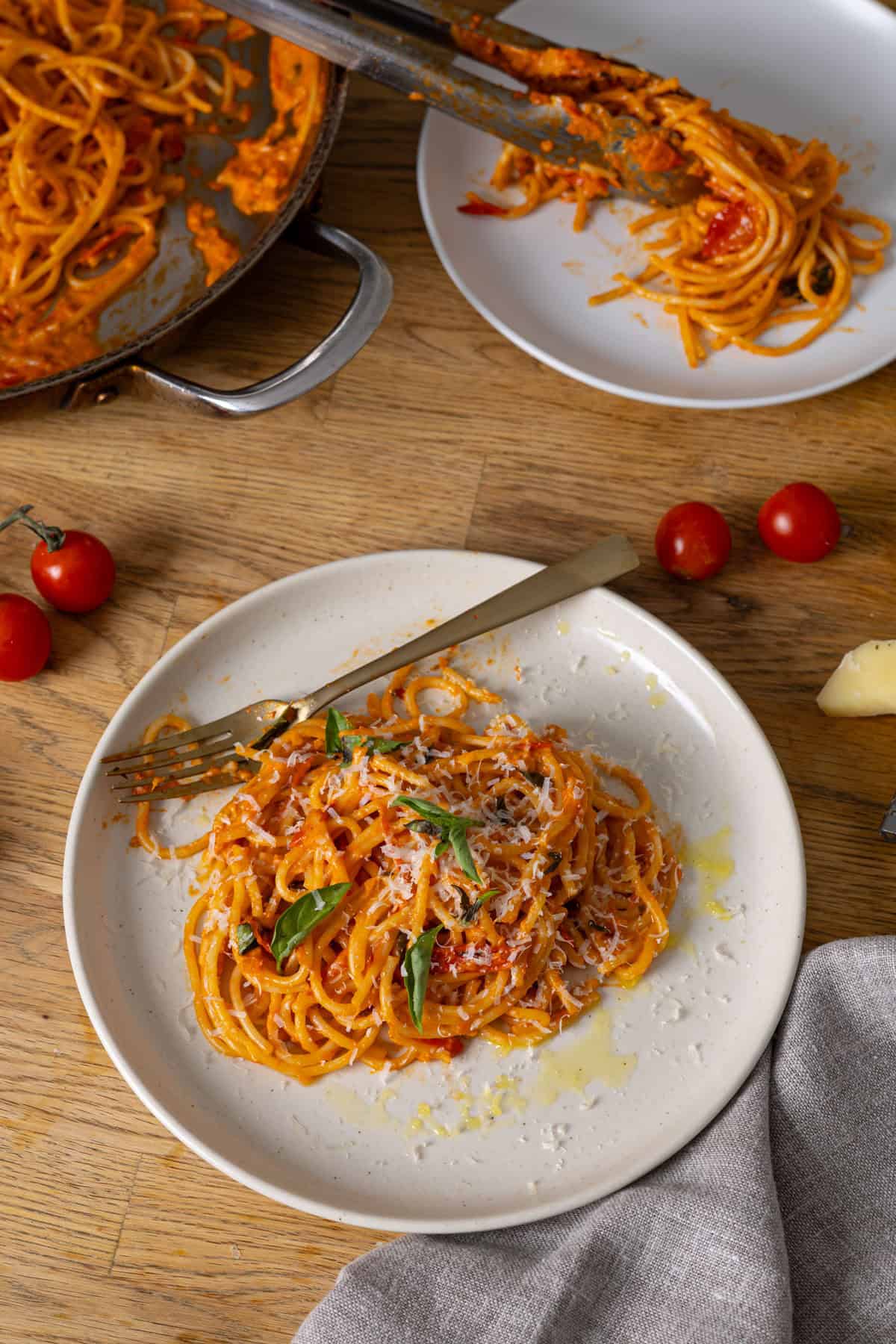 Two servings of pasta with cherry tomato sauce on a butcher block countertop.