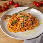 A serving of cherry tomato sauce with spaghetti on a small plate and a skillet with cherry tomatoes in the background.