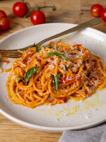 A serving of cherry tomato sauce with spaghetti on a small plate and a skillet with cherry tomatoes in the background.