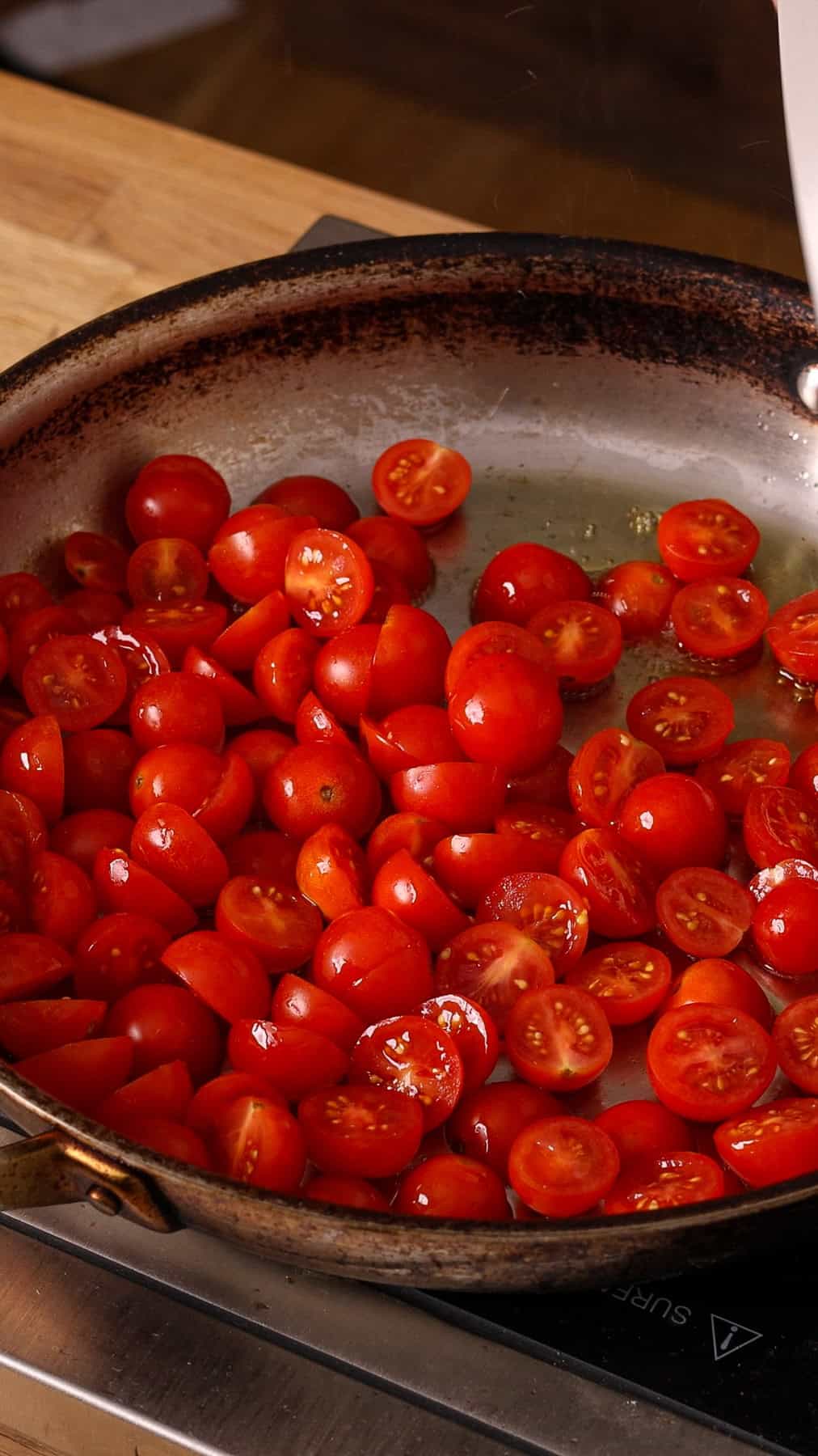 Cherry tomatoes cooking in a large skillet with some olive oil.