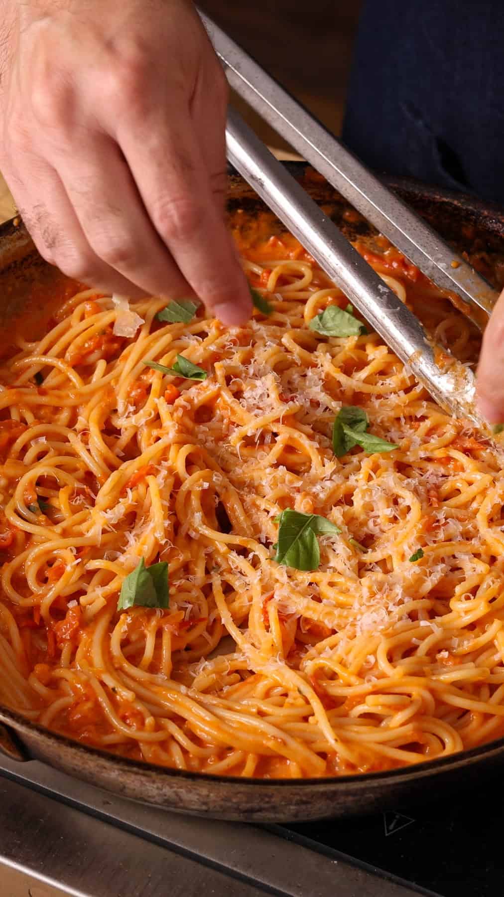 Adding basil to a skillet with spaghetti and cherry tomato sauce.