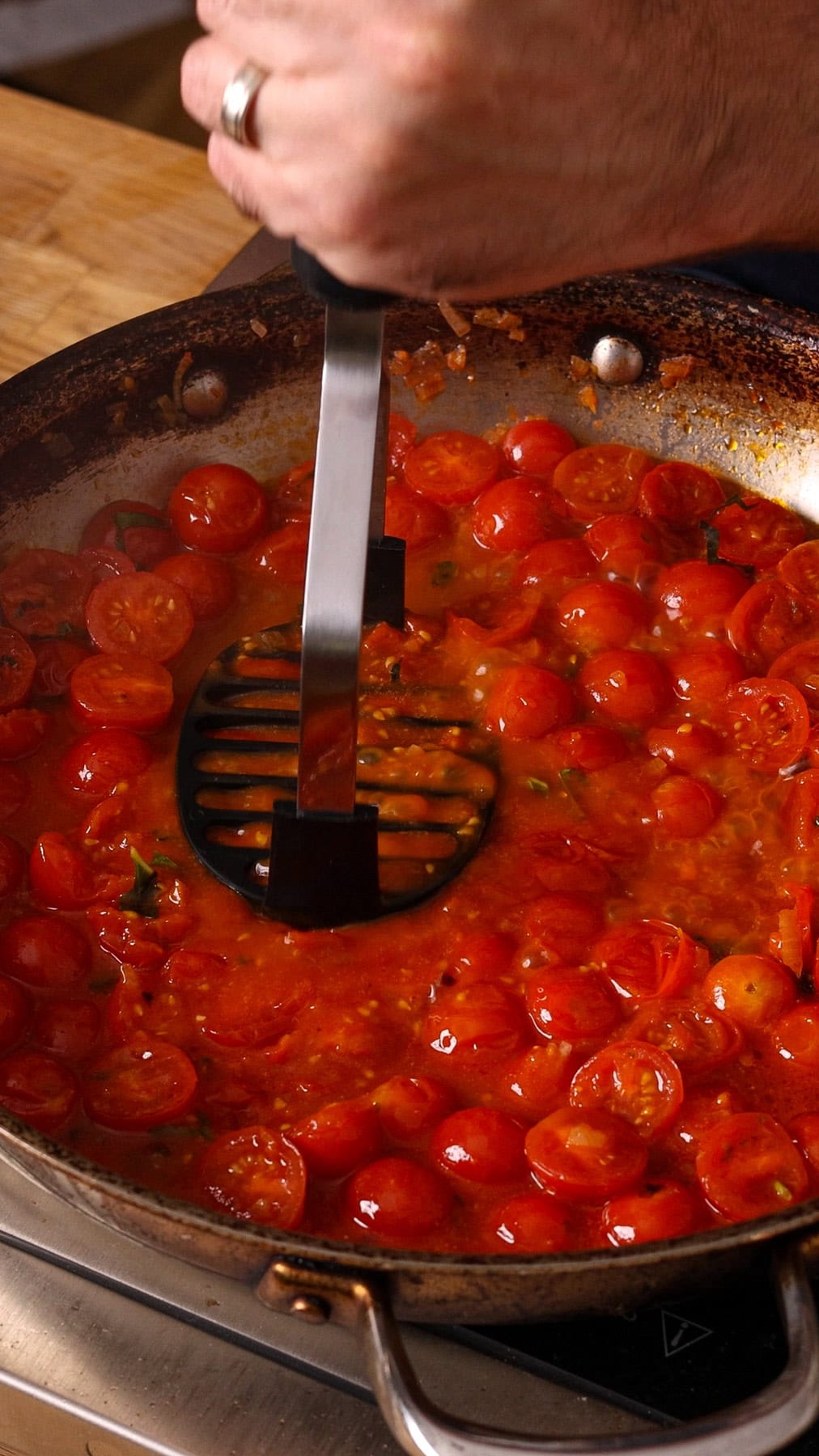Cooked cherry tomatoes getting mashed in a large skillet.