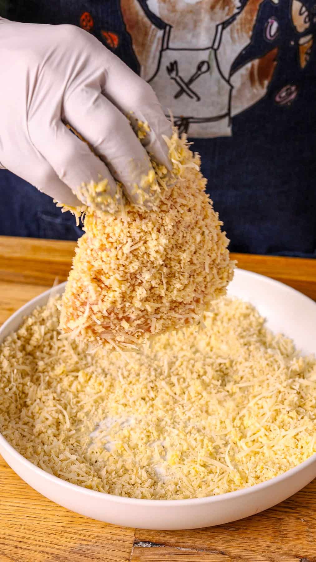 Chicken breasts getting coated in breadcrumbs.