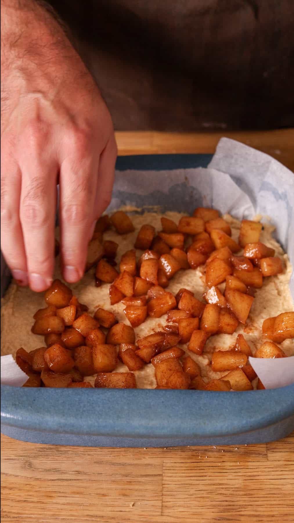 Caramelized apples getting placed on top of applesauce cake.
