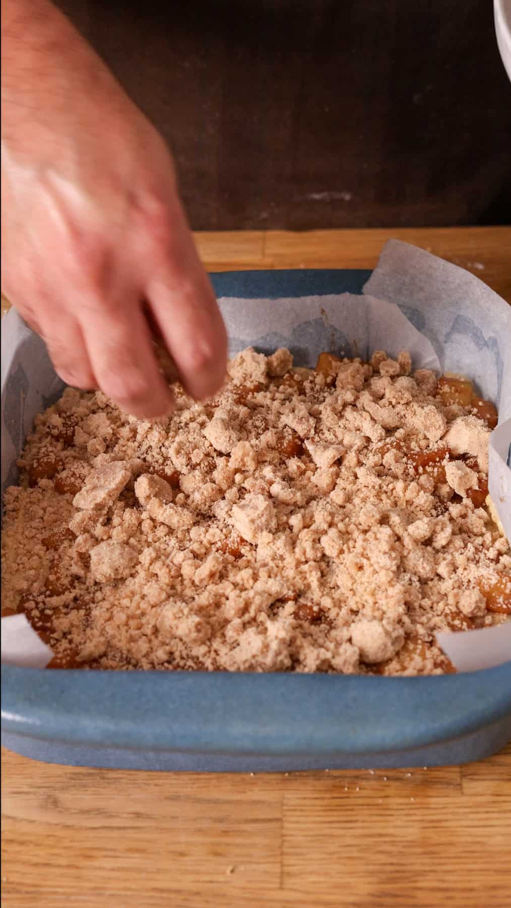 Crumb topping getting placed on top of an applesauce coffee cake.