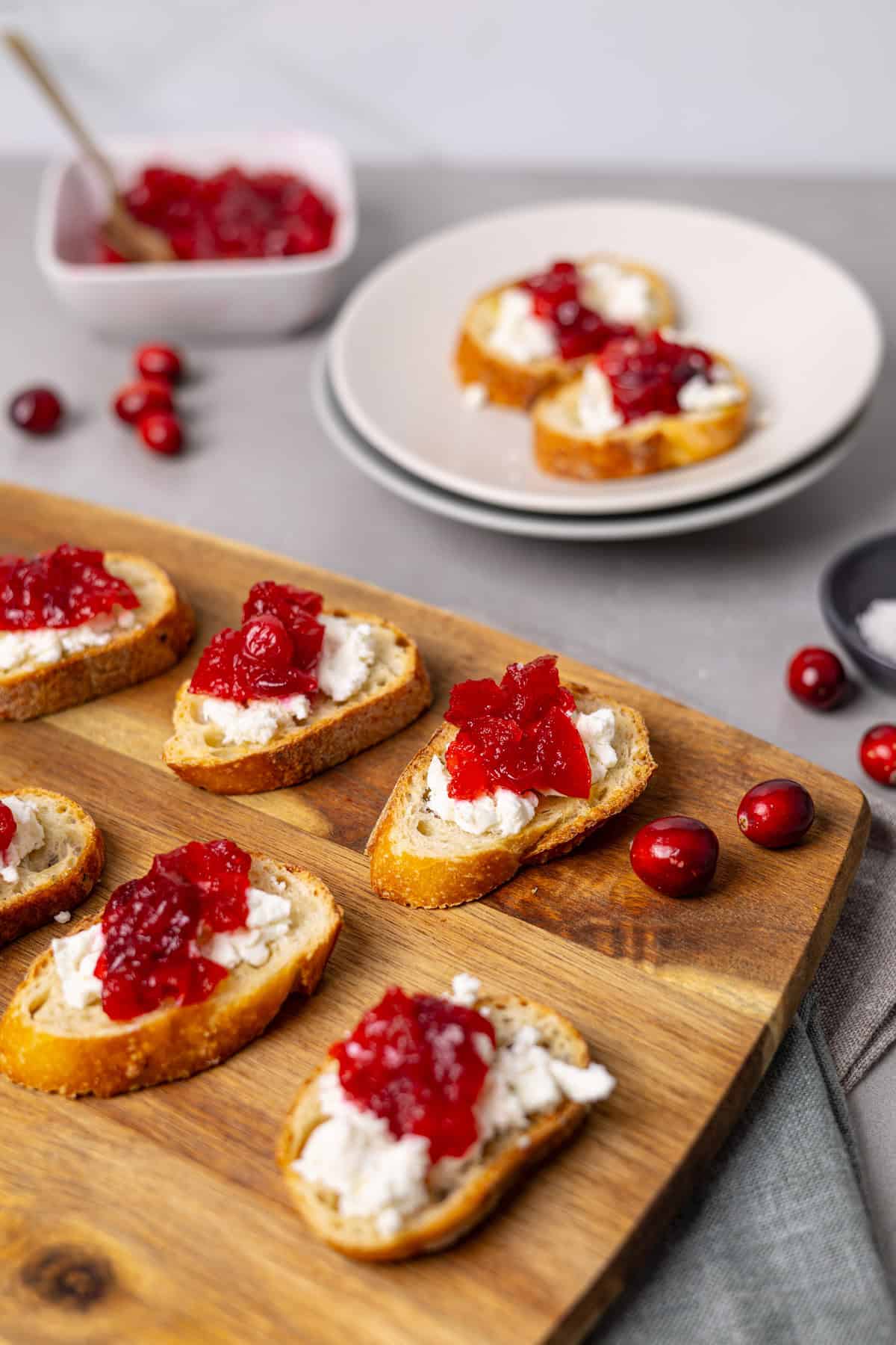 A cutting board and plate with cranberry and goat cheese crostini.