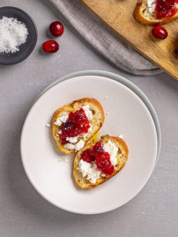 A close-up of cranberry and goat cheese crostini on a small plate.