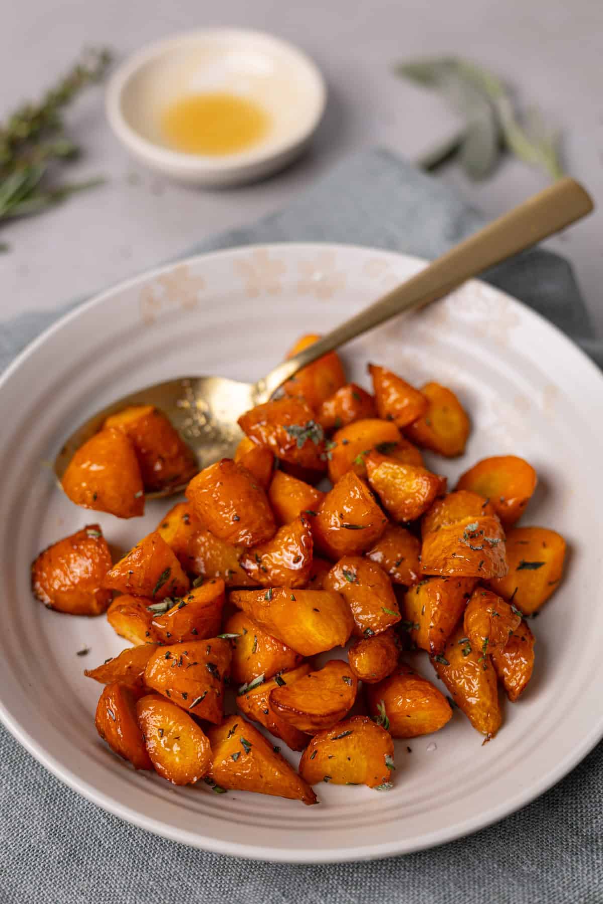 A closeup shot of a bowl of air fryer honey roasted carrots with herbs in the background.