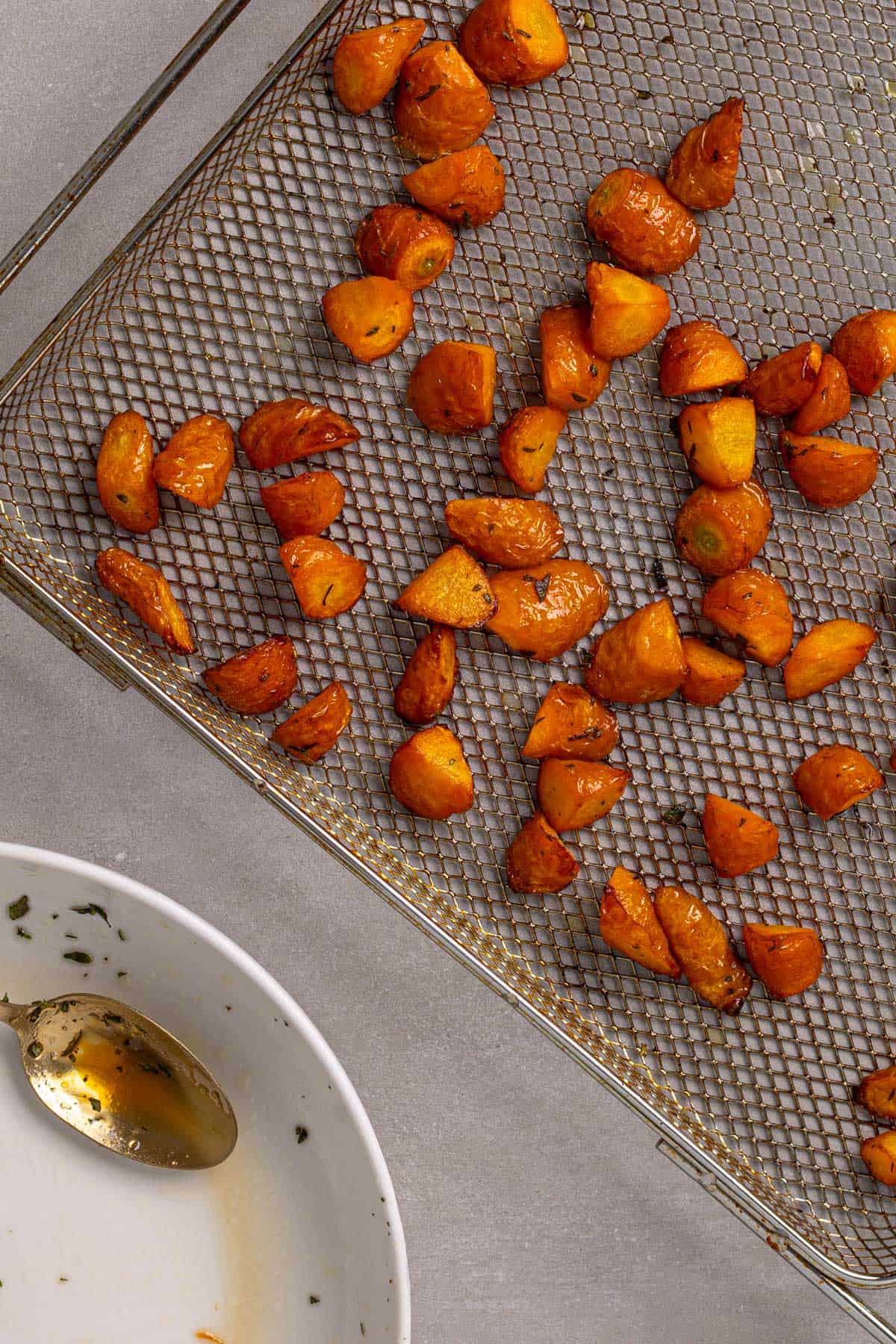An air fryer basket with honey roasted carrots on a gray table.