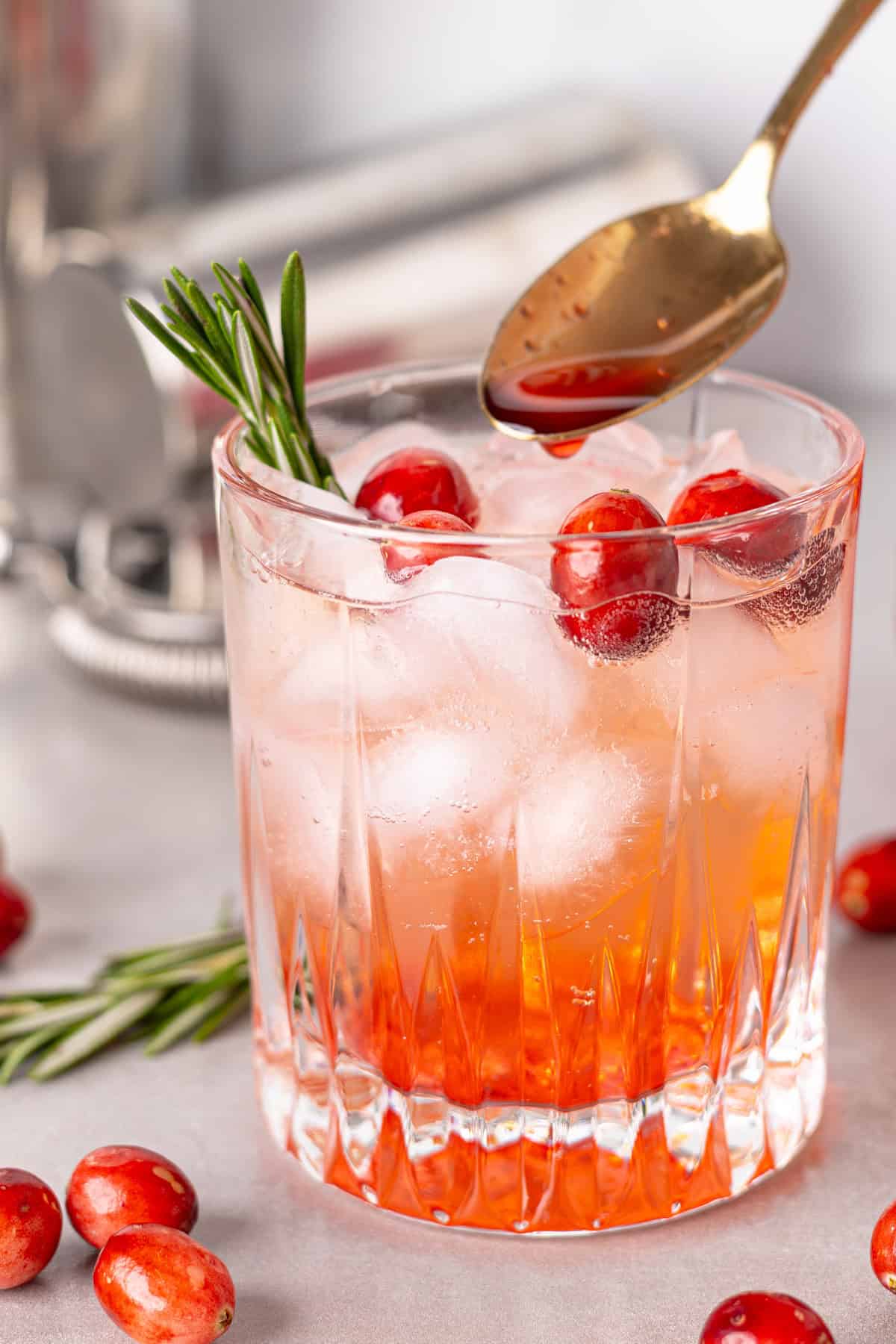 A glass of a cranberry cocktail with a spoon pouring in cranberry simple syrup.