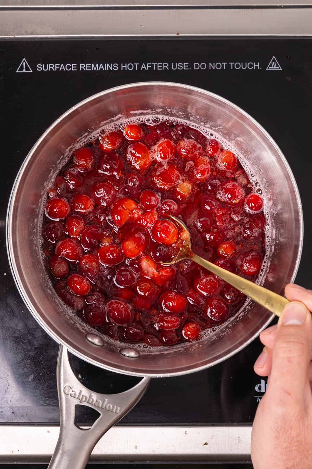 A small saucepan with cranberry simple syrup and a spoon scooping out the burst cranberries.