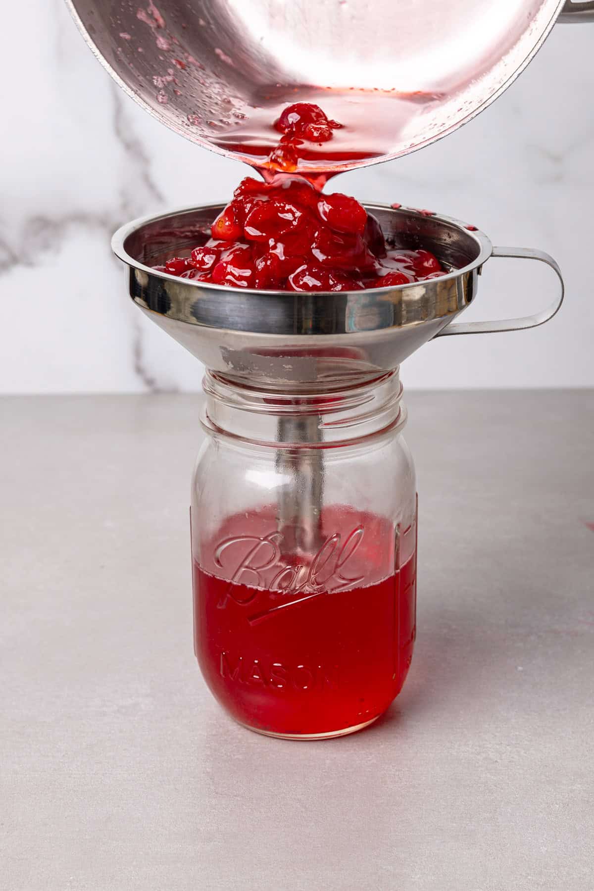 Cranberry simple syrup getting strained into a mason jar.