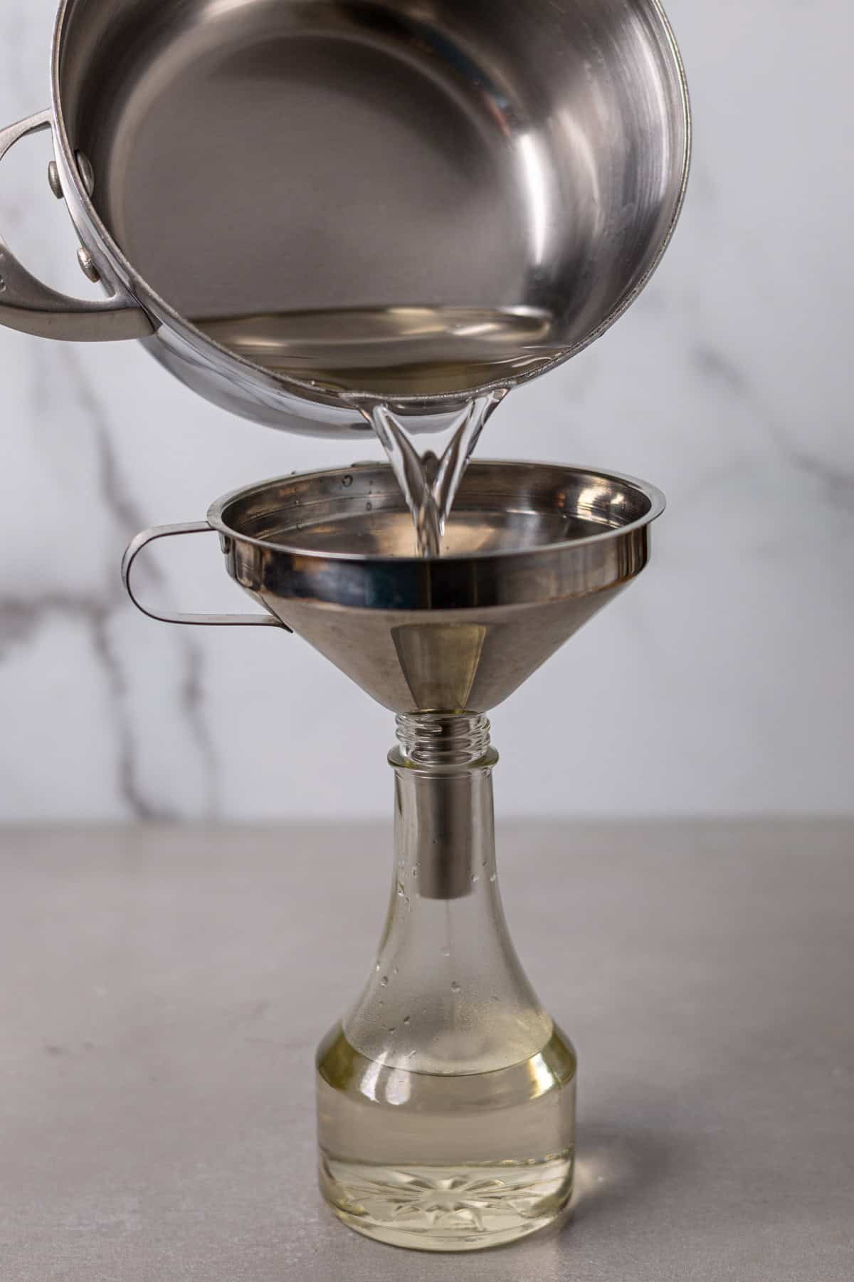 Simple syrup pouring from a saucepan into a small glass bottle.