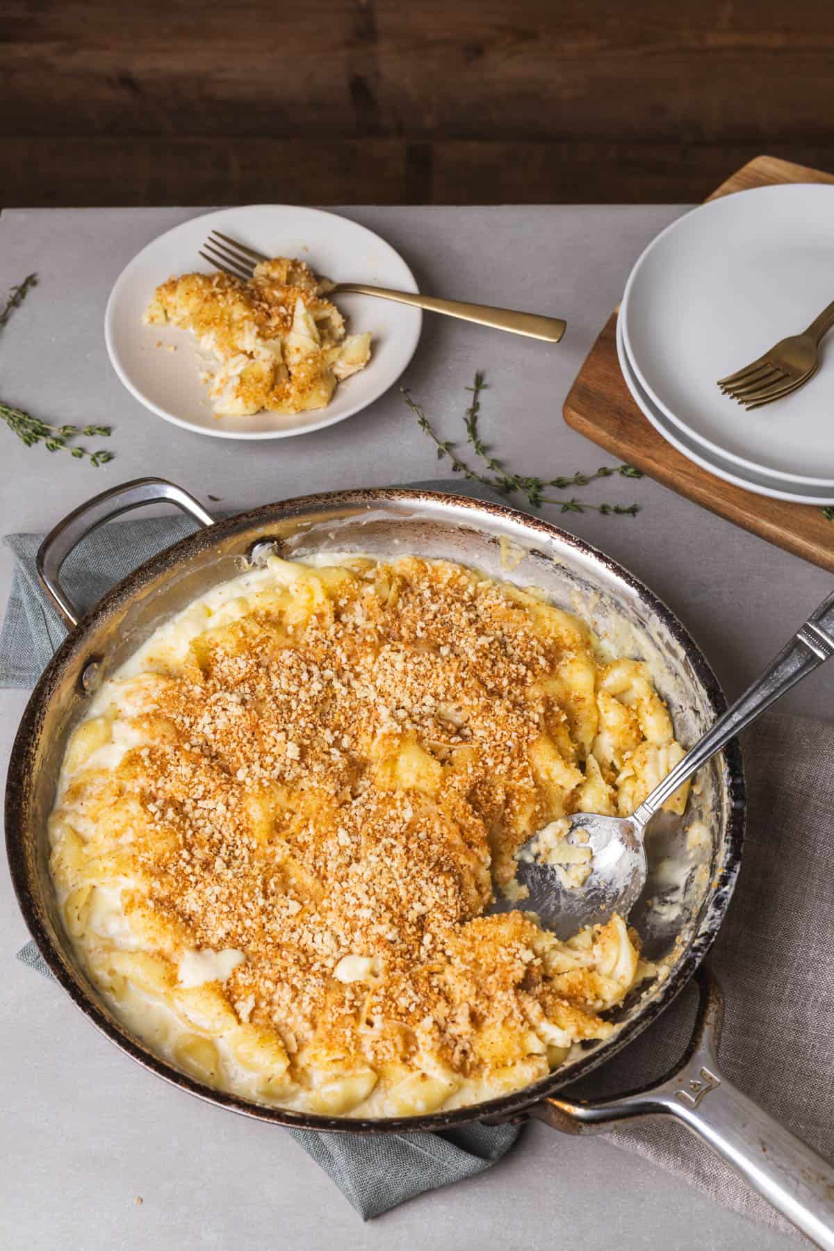A skillet on a gray table with gouda mac and cheese topped with gold brown panko breadcrumbs. 