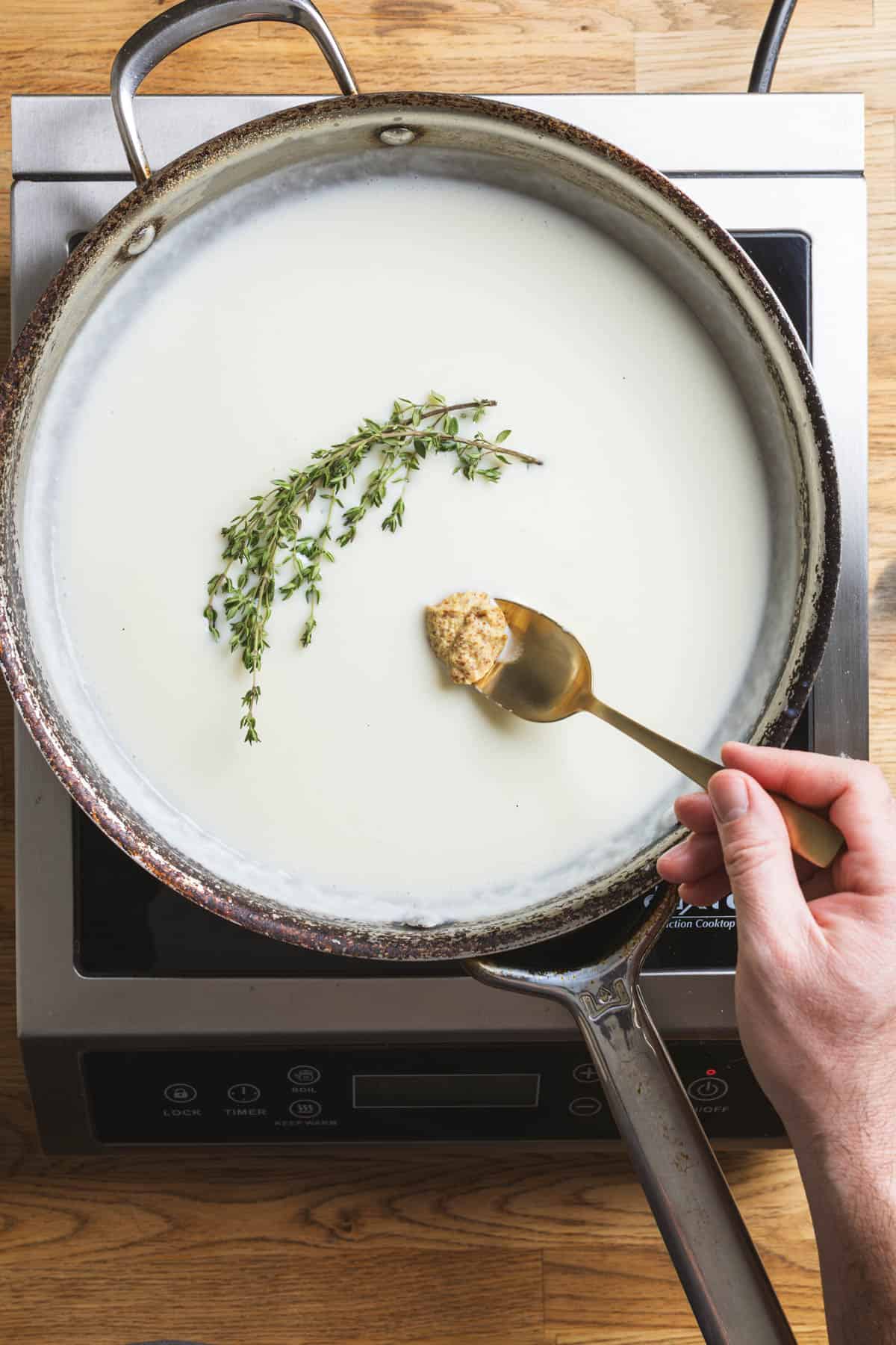 A large skillet with hot milk, thyme, and dijon mustard.