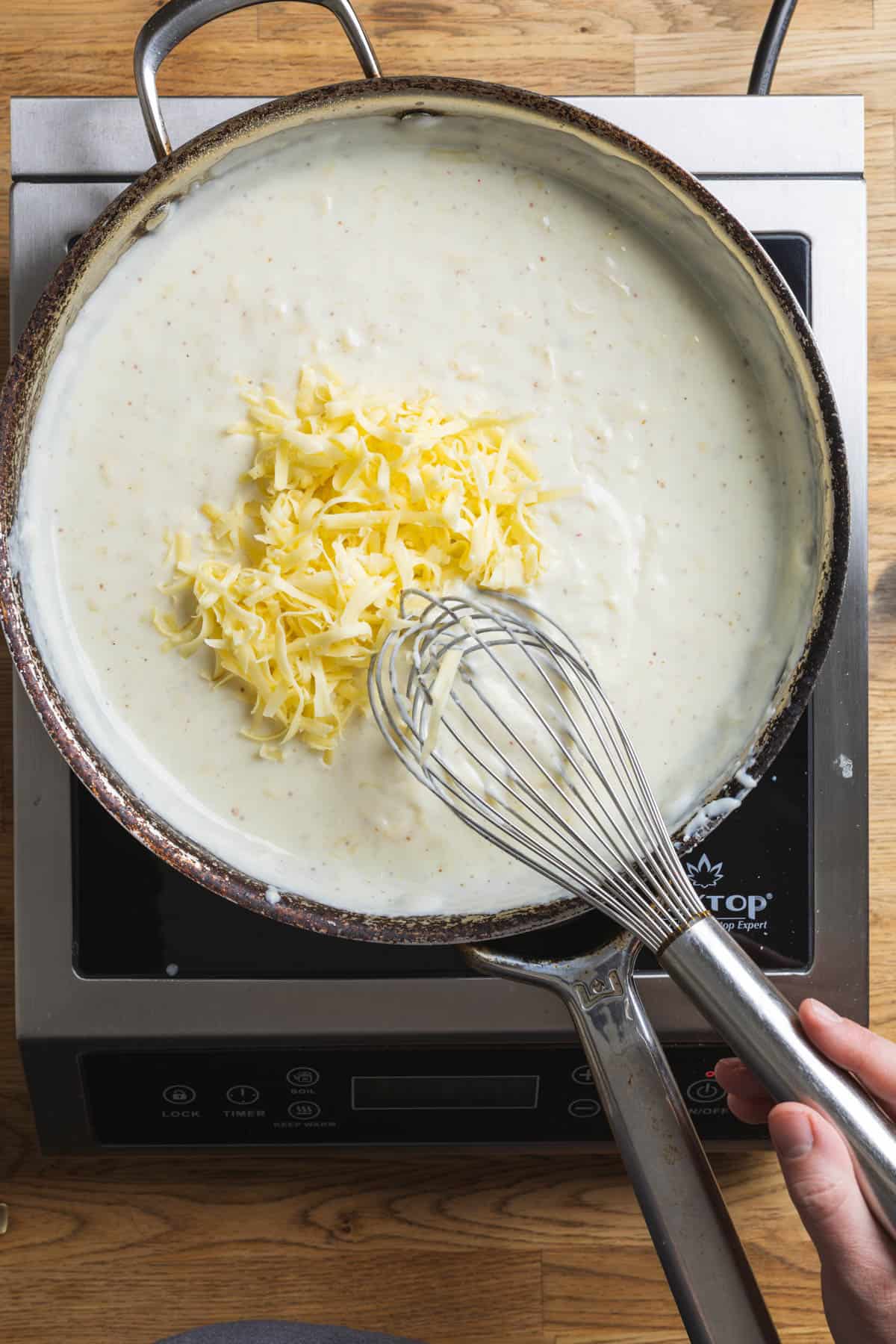 Cheese getting whisked into a cream sauce for a gouda mac and cheese .