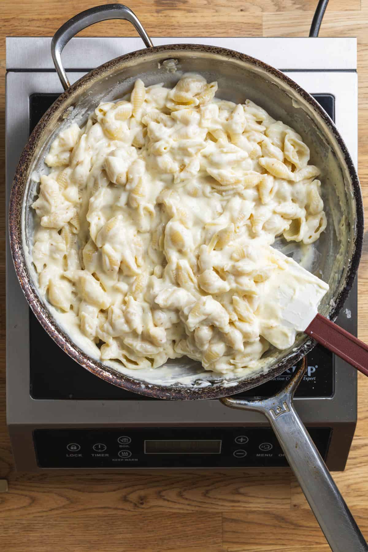 Pasta added to gouda cheese sauce in a large skillet.